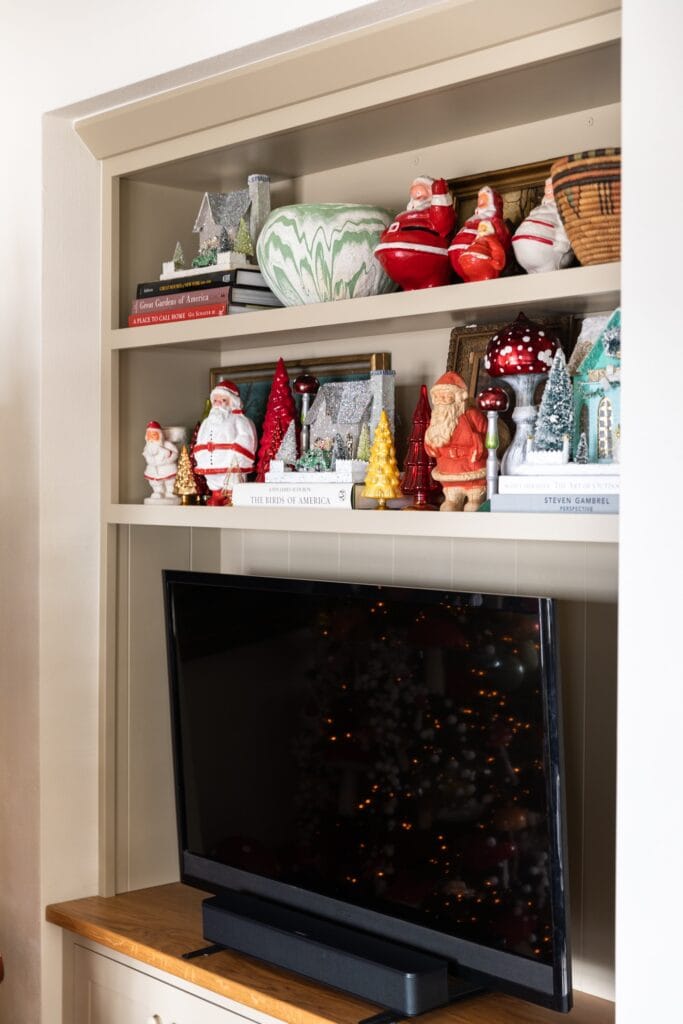 TV cabinet with shelves above adorned with Christmas Santas and glass Christmas trees