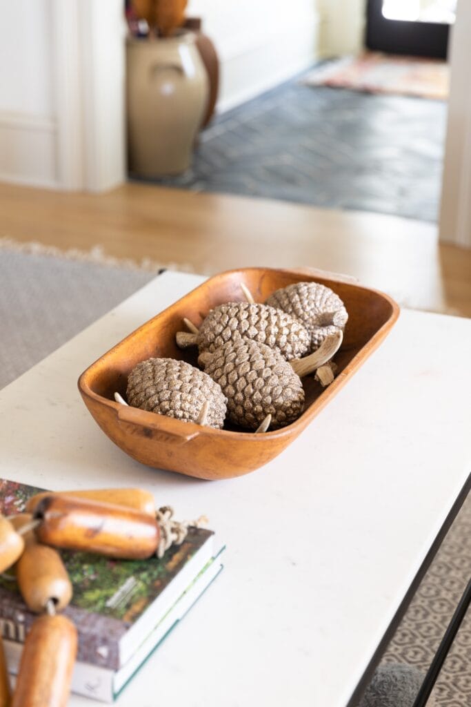 Marble coffee table with brown wooden bowl filled with sparkling pinecones