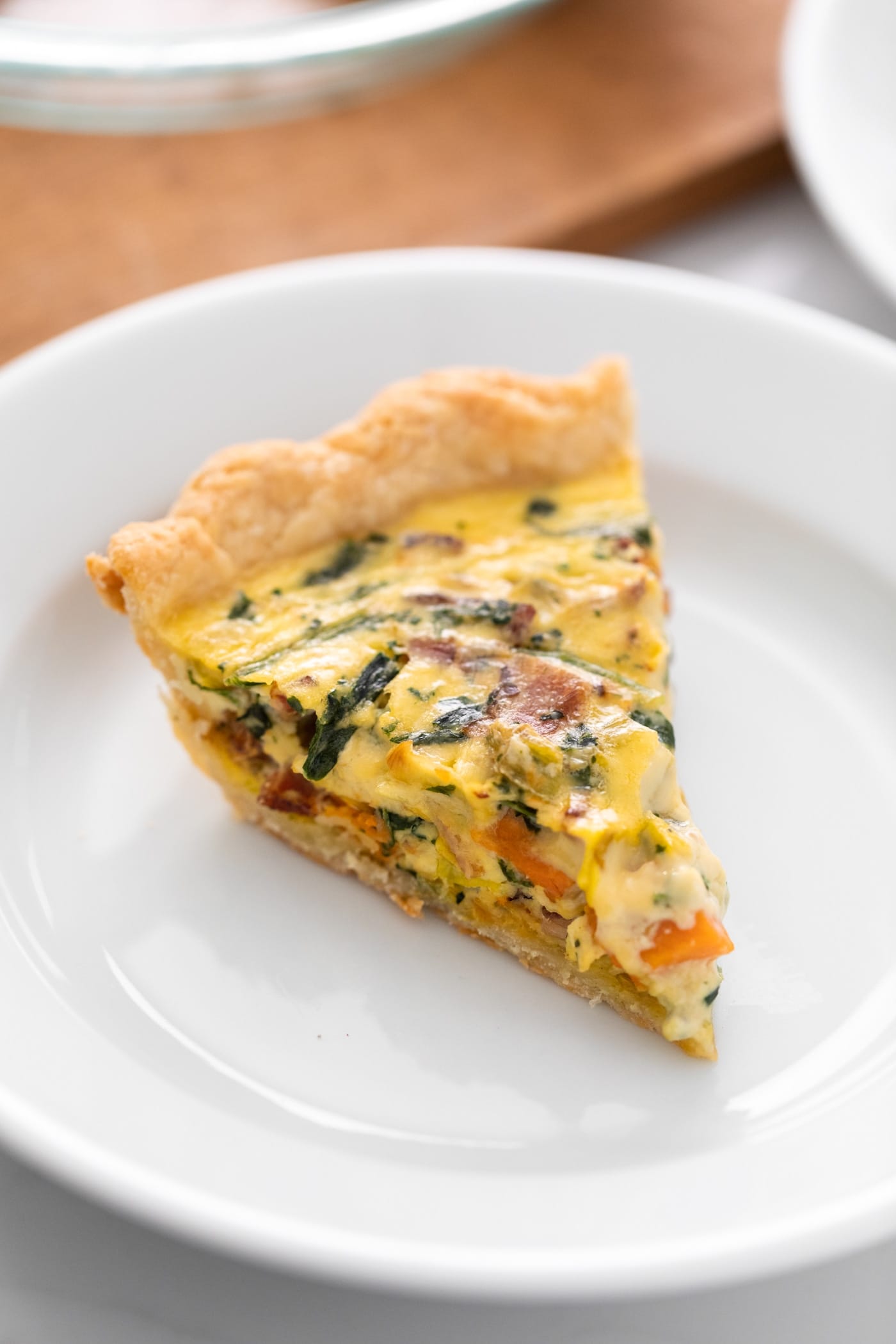 Slice of yellow colored quiche sitting on white plate with wood surface in background
