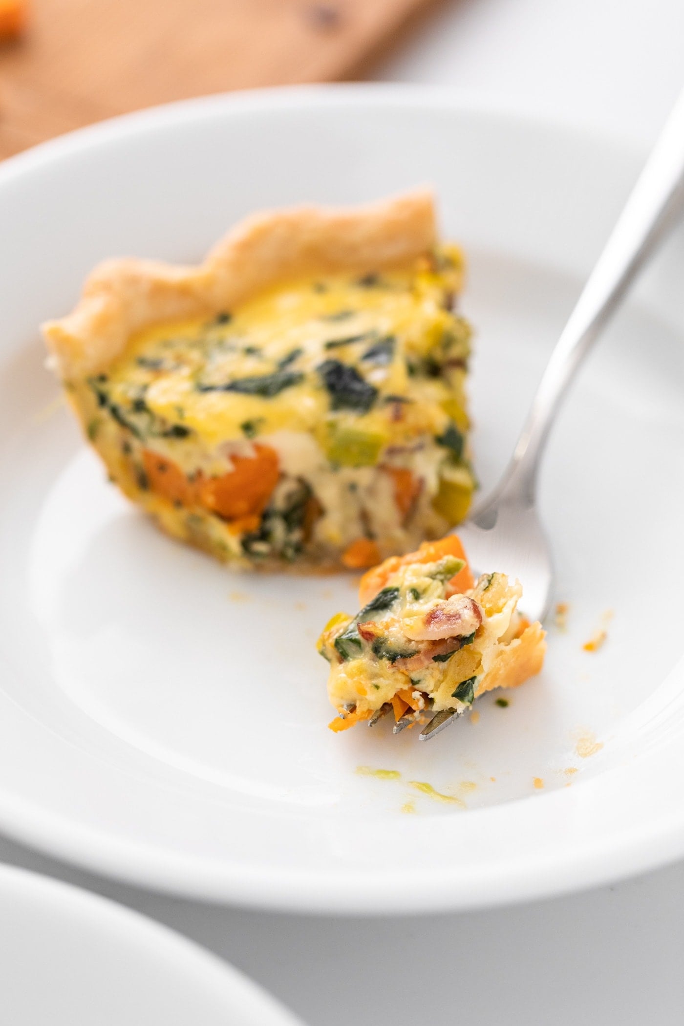 White plate containing piece of quiche with piece cut out sitting on fork