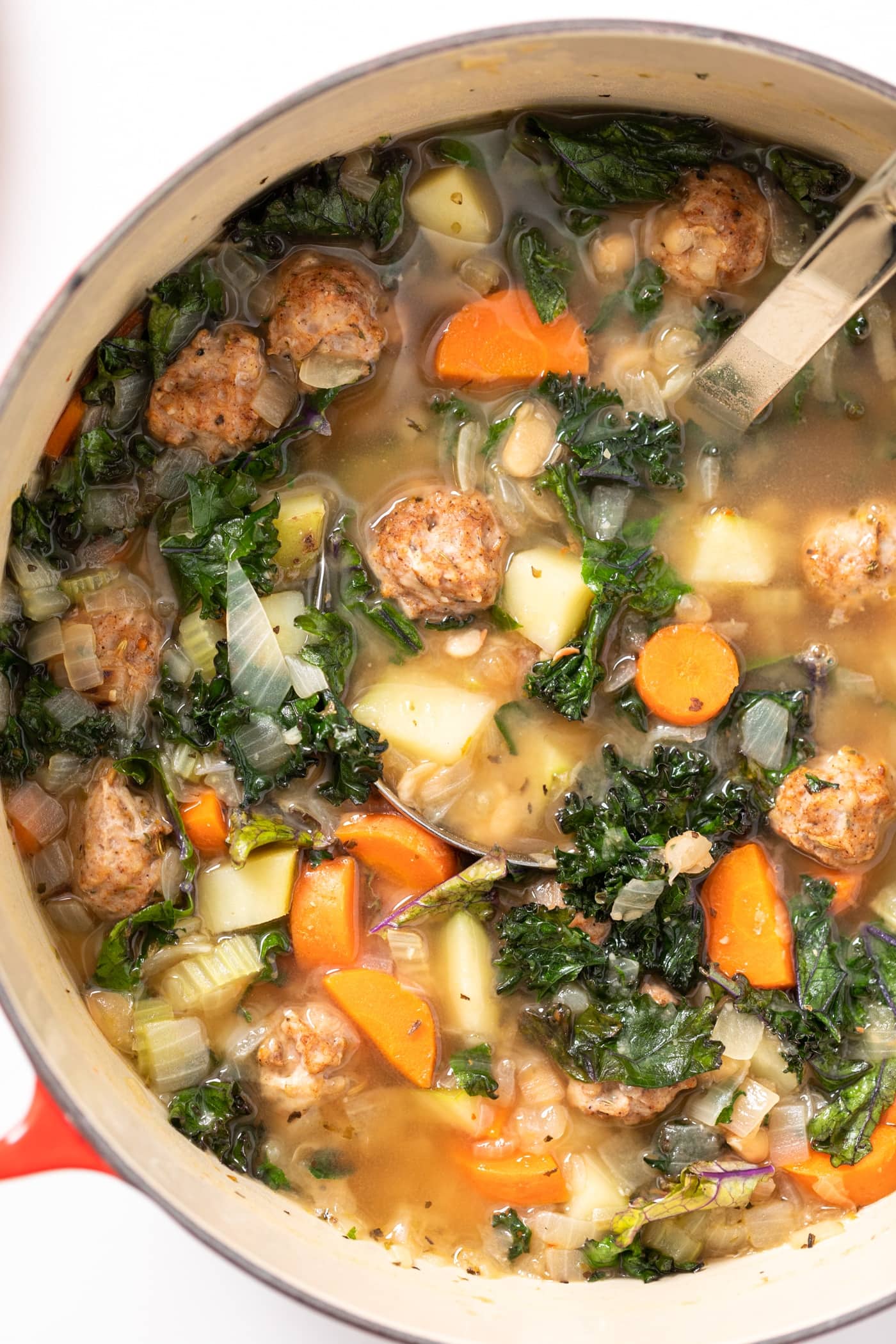 Top down view of Dutch oven filled with light brown colored soup filled with carrots and potatoes and sausage balls
