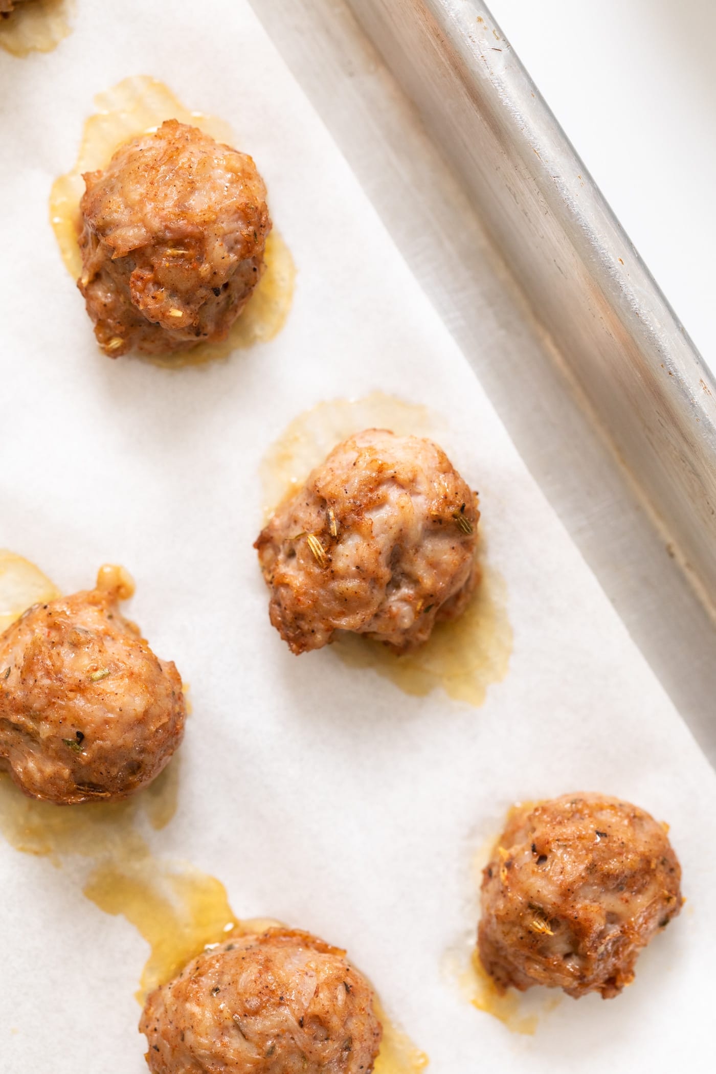 Top down view of brown colored chicken sausage meatballs sitting on piece of white parchment on a baking sheet