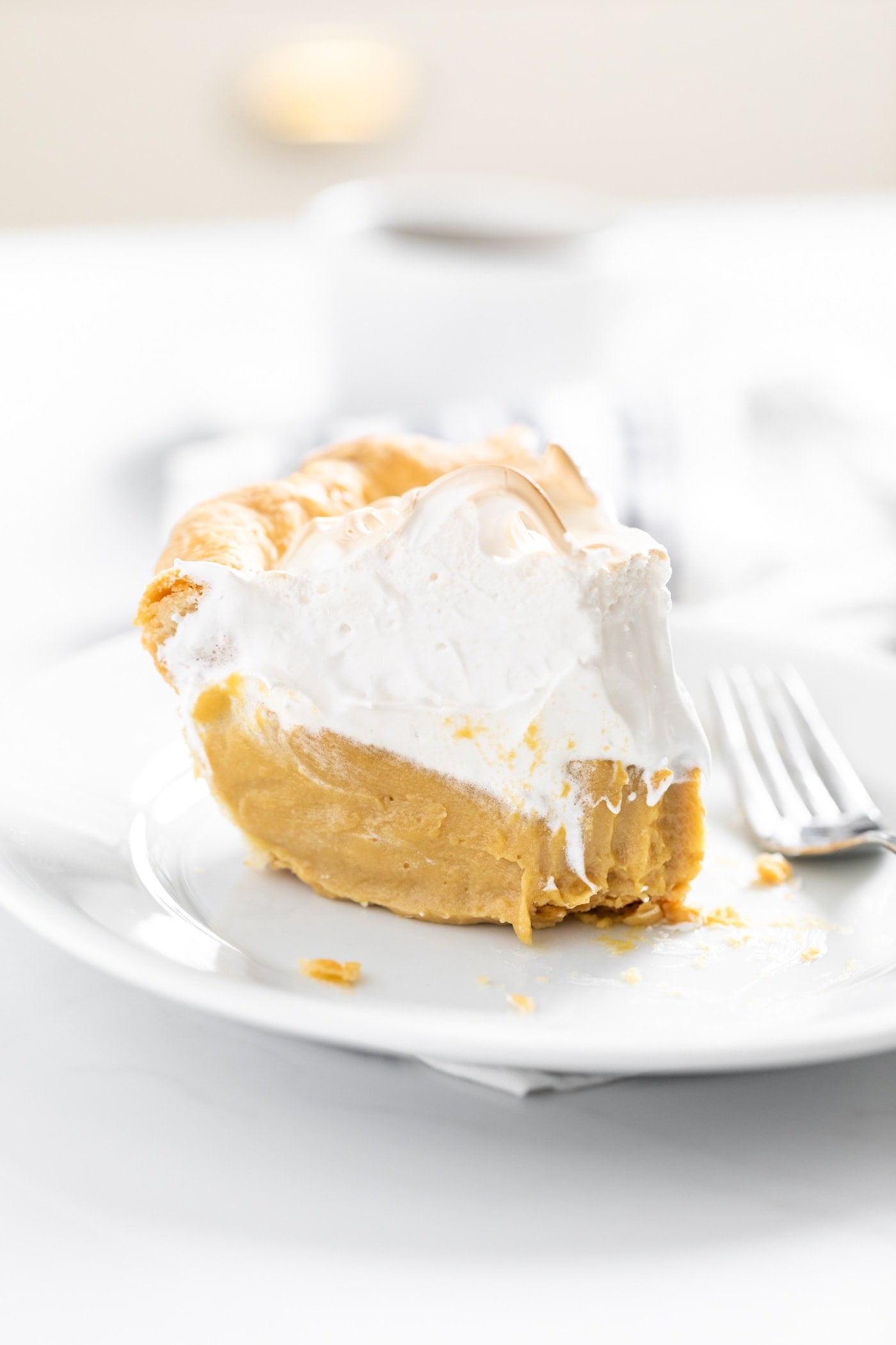 Close up view of piece of butterscotch pie topped with creme brûlée frosting sitting on white plate all on white countertop with mug in background