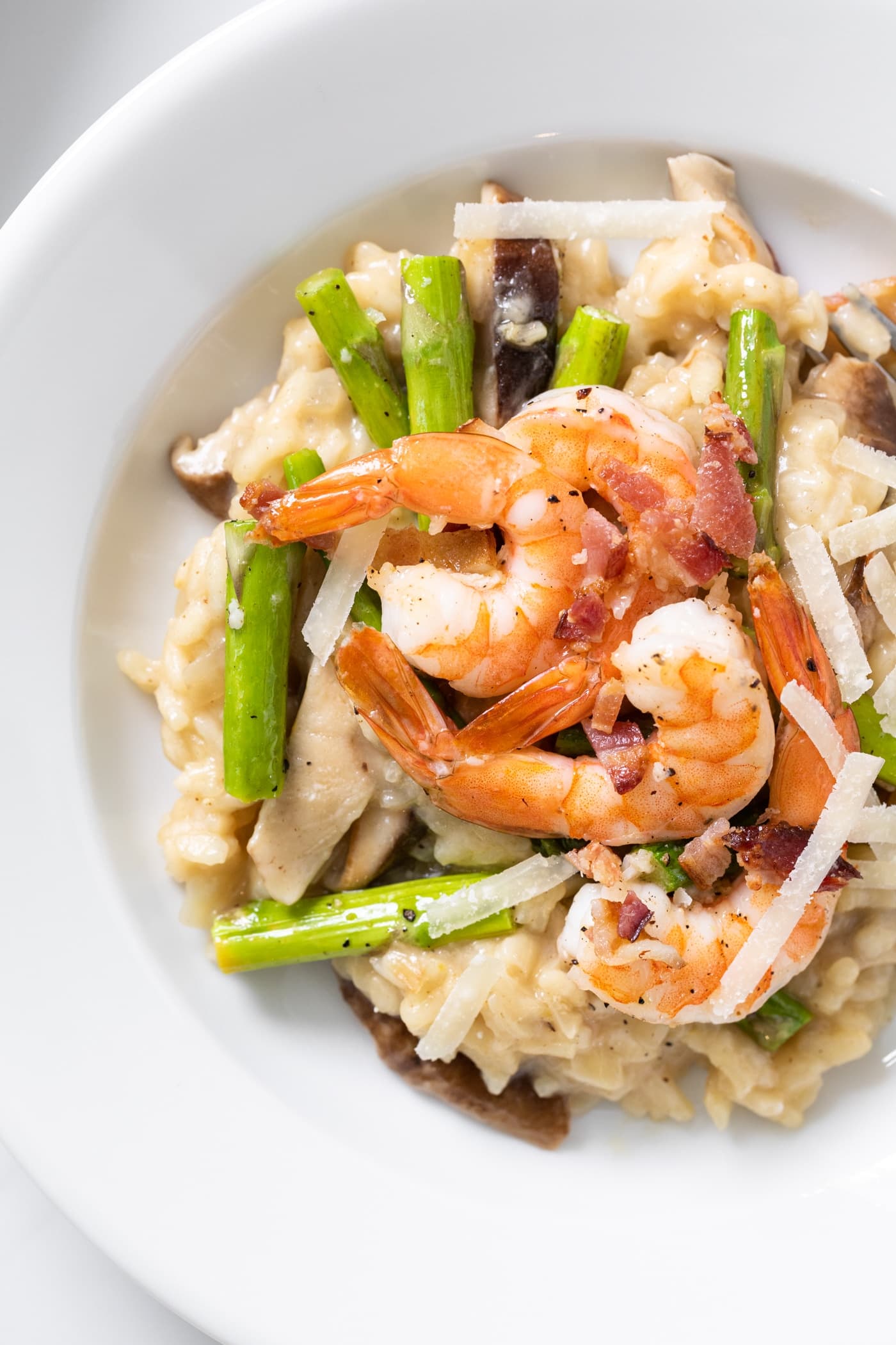Top down close up view of risotto sitting on white plate topped with asparagus and pink colored shrimp pieces
