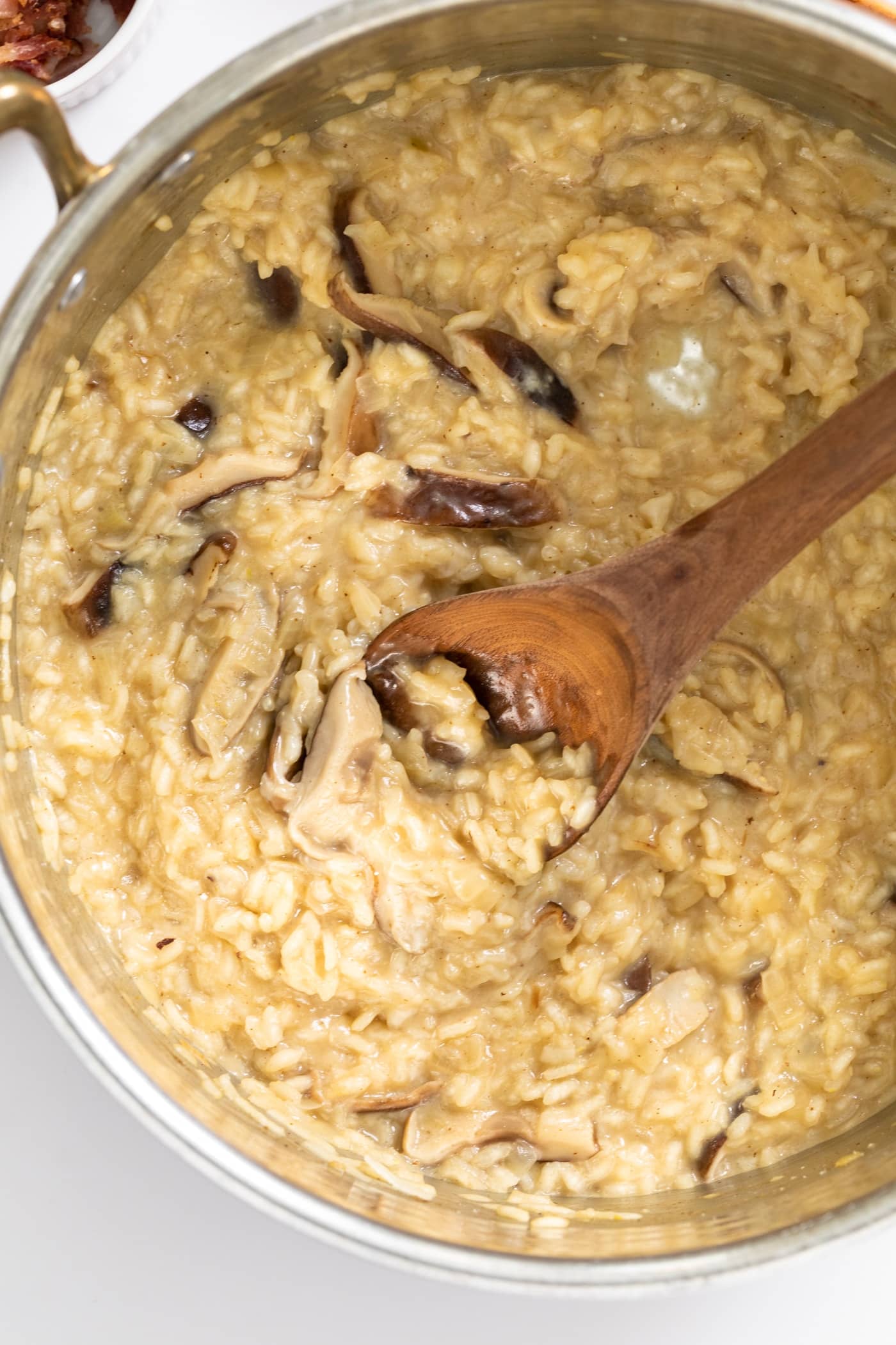 Top down view of creamy yellow colored risotto sitting in copper colored kettle with wooden spoon sitting inside