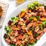 Top down view of salmon salad sitting on white platter with serving spoons sitting beside
