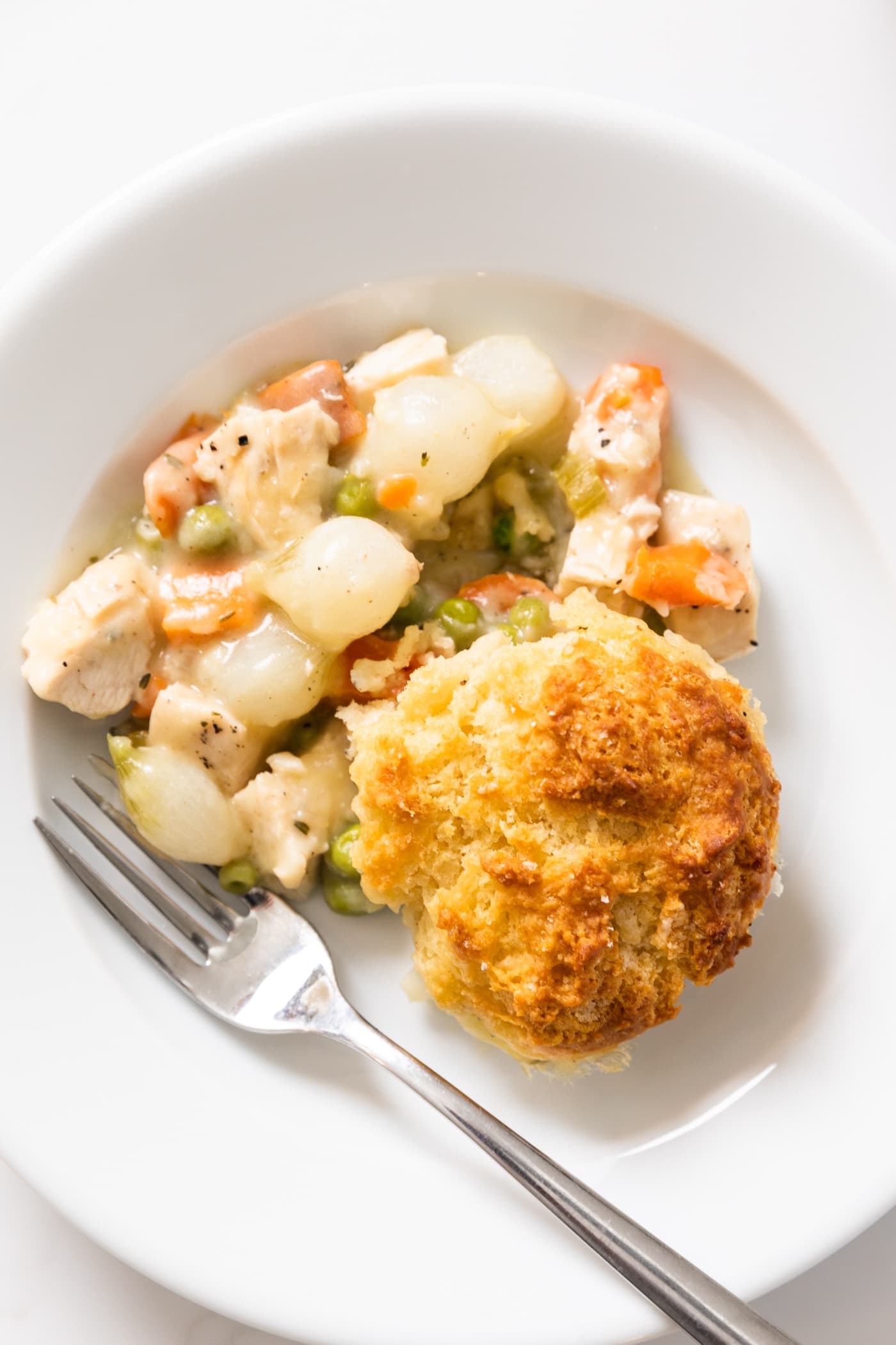 Top down view of white plate holding a thickened sauce with vegetables sitting in mixture topped with a biscuit