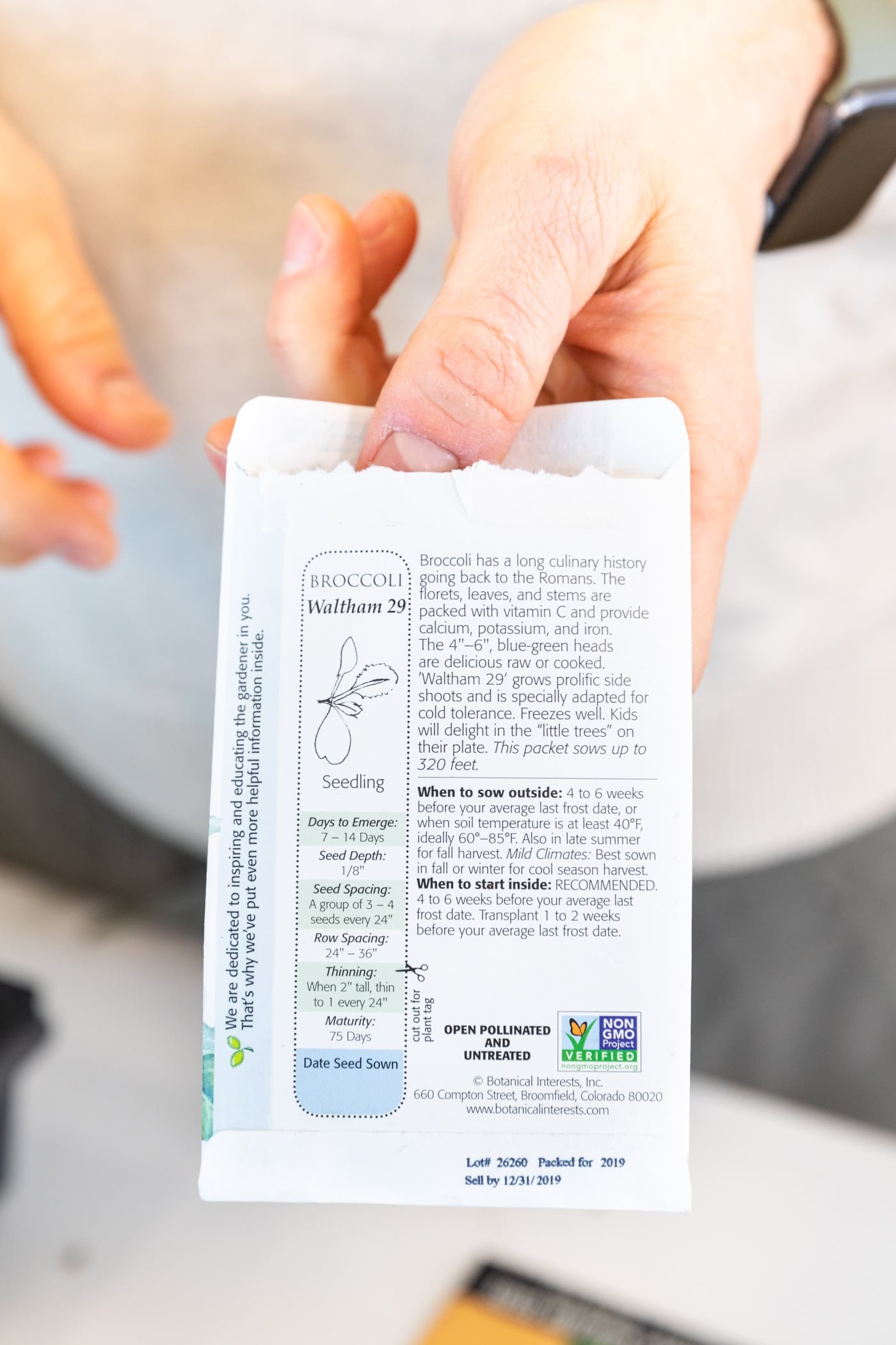 Hand holding seed packet with lots of writing on the back in front of a white countertop