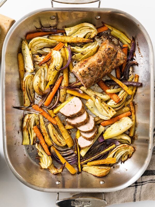 Top down view of steel pan with roasted vegetables sitting in the bottom with pork tenderloin with slices cut
