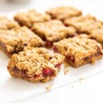 Nine square pieces of raspberry crumb bars sitting one white piece of parchment on white countertop