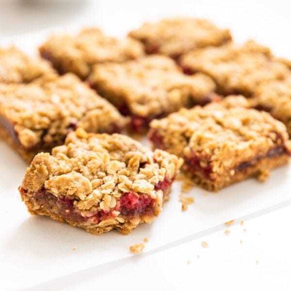 Nine square pieces of raspberry crumb bars sitting one white piece of parchment on white countertop