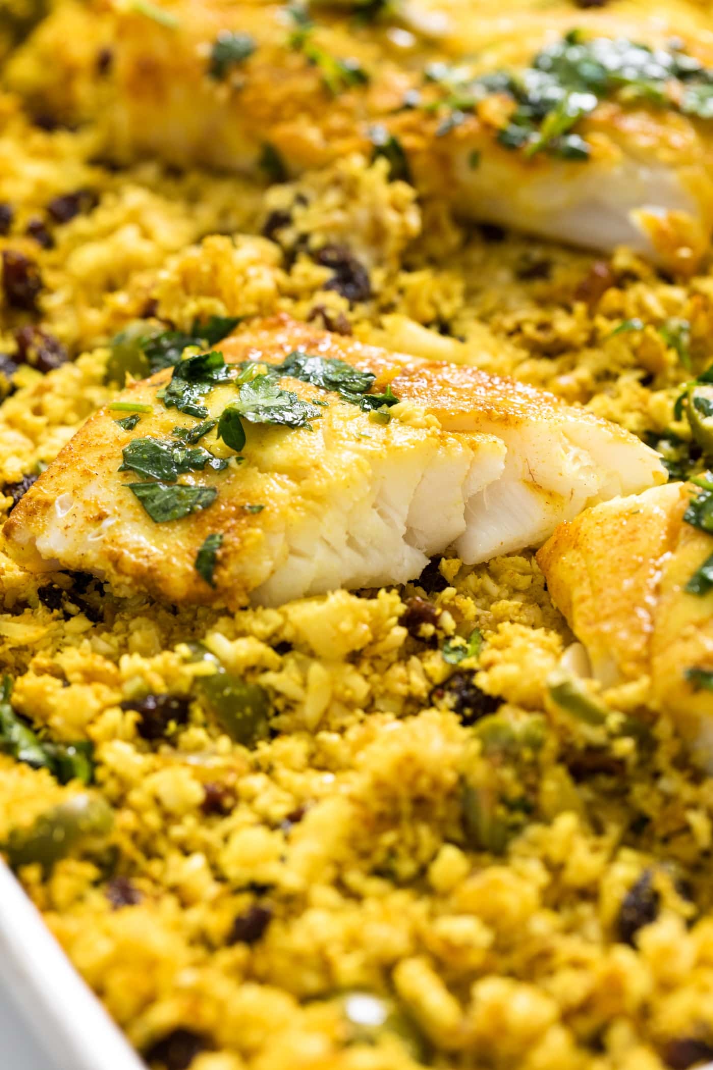 Piece of fish split in half sitting on bed of yellow cauliflower rice with green mix on top