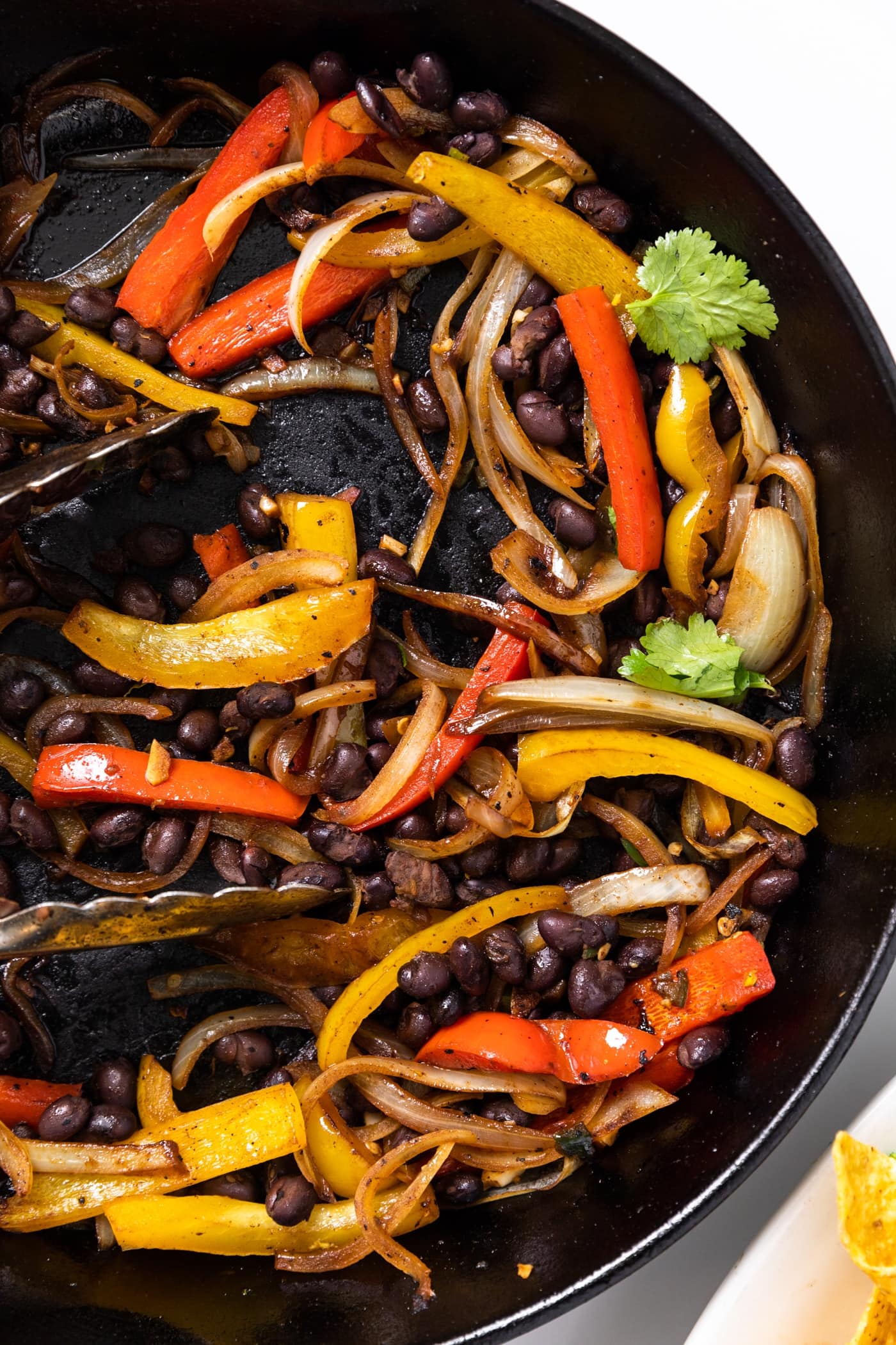 Top down view of black skillet filled with red and yellow peppers along with black beans all on white countertop
