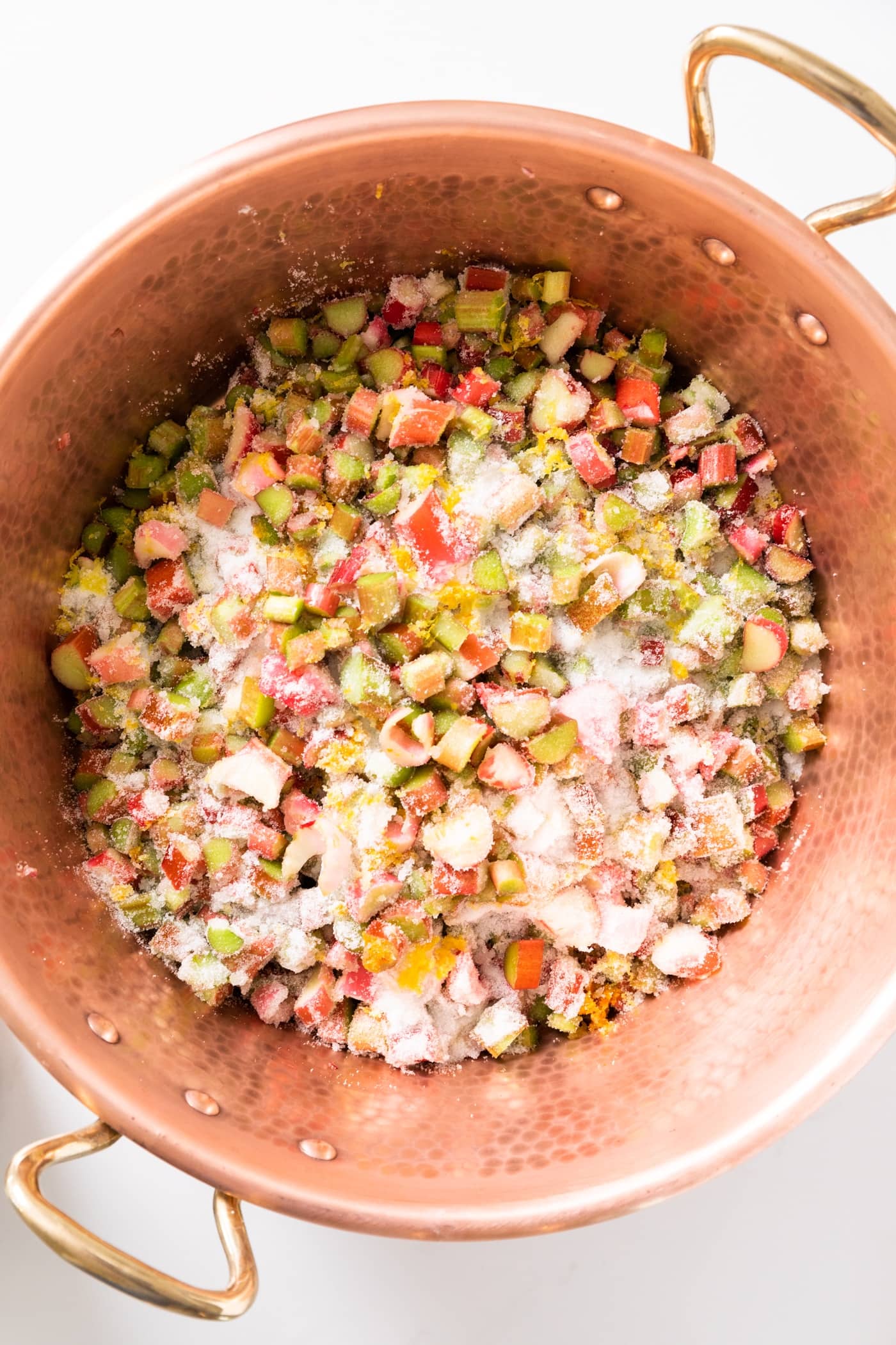 Top down view of copper jam pan filled with chopped raw rhubarb with sugar sprinkled on top