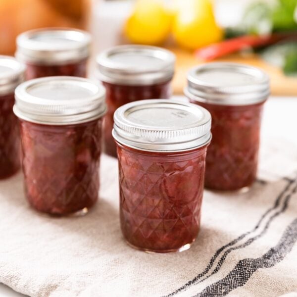 Glass pint jars filled with red colored rhubarb jam sitting on drying clothing all on white countertop