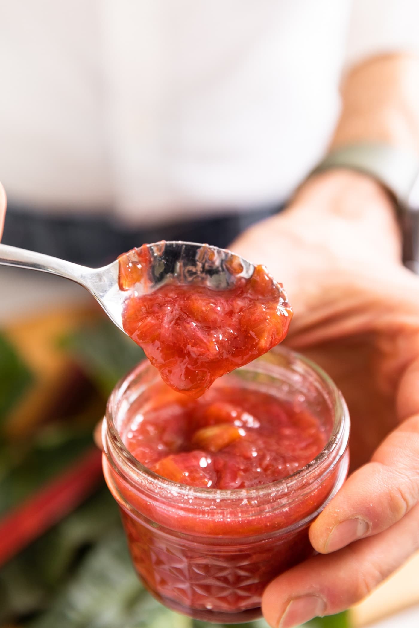 Spoon holding red colored rhubarb jam dripping into jam container