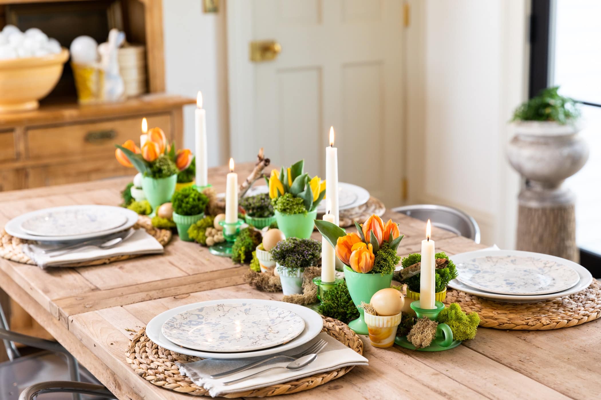 Wooden table spread spread with freshly colored tulip flowers in green vases with plates set around table