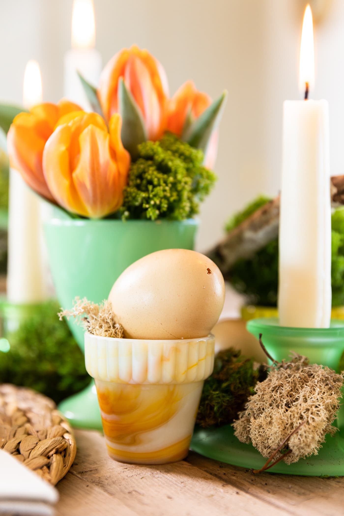 Light brown colored preserved egg sitting in small white and orange container on wood table with orange tulips in a green glass in background