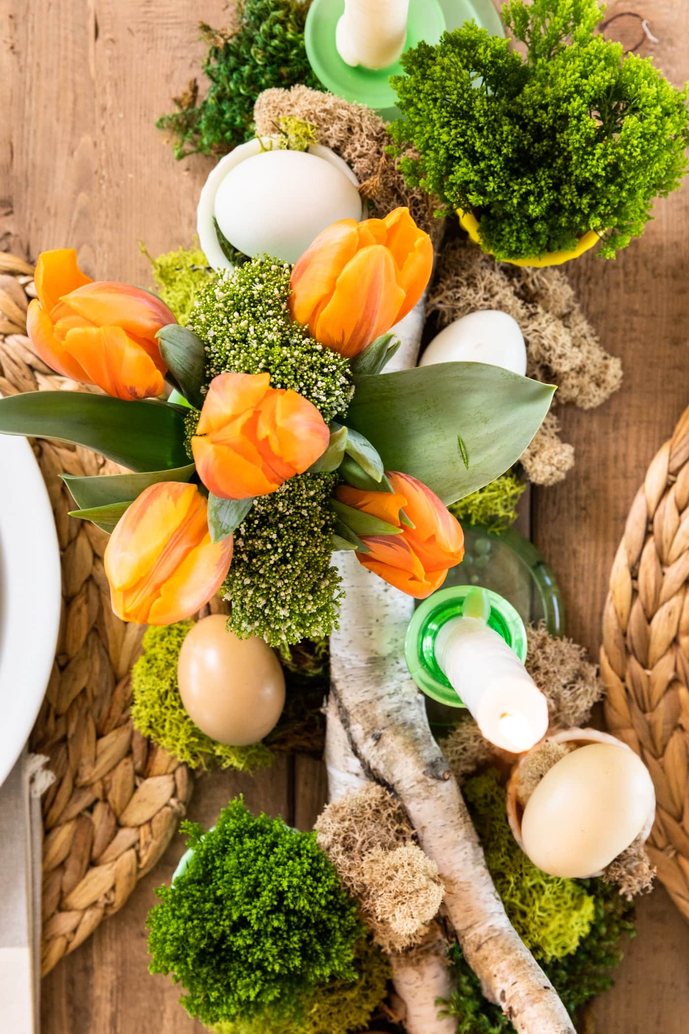 Top down view of tabletop with green moss, orange tulips, birch log, and set with plates