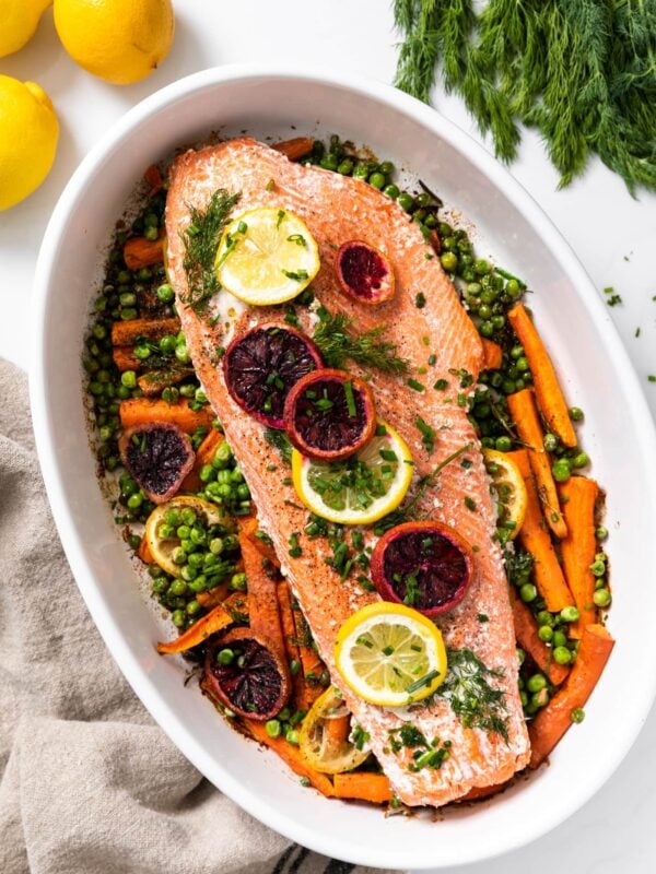Top down view of white platter filled with carrots topped with a salmon filet with lemon and orange slices on top