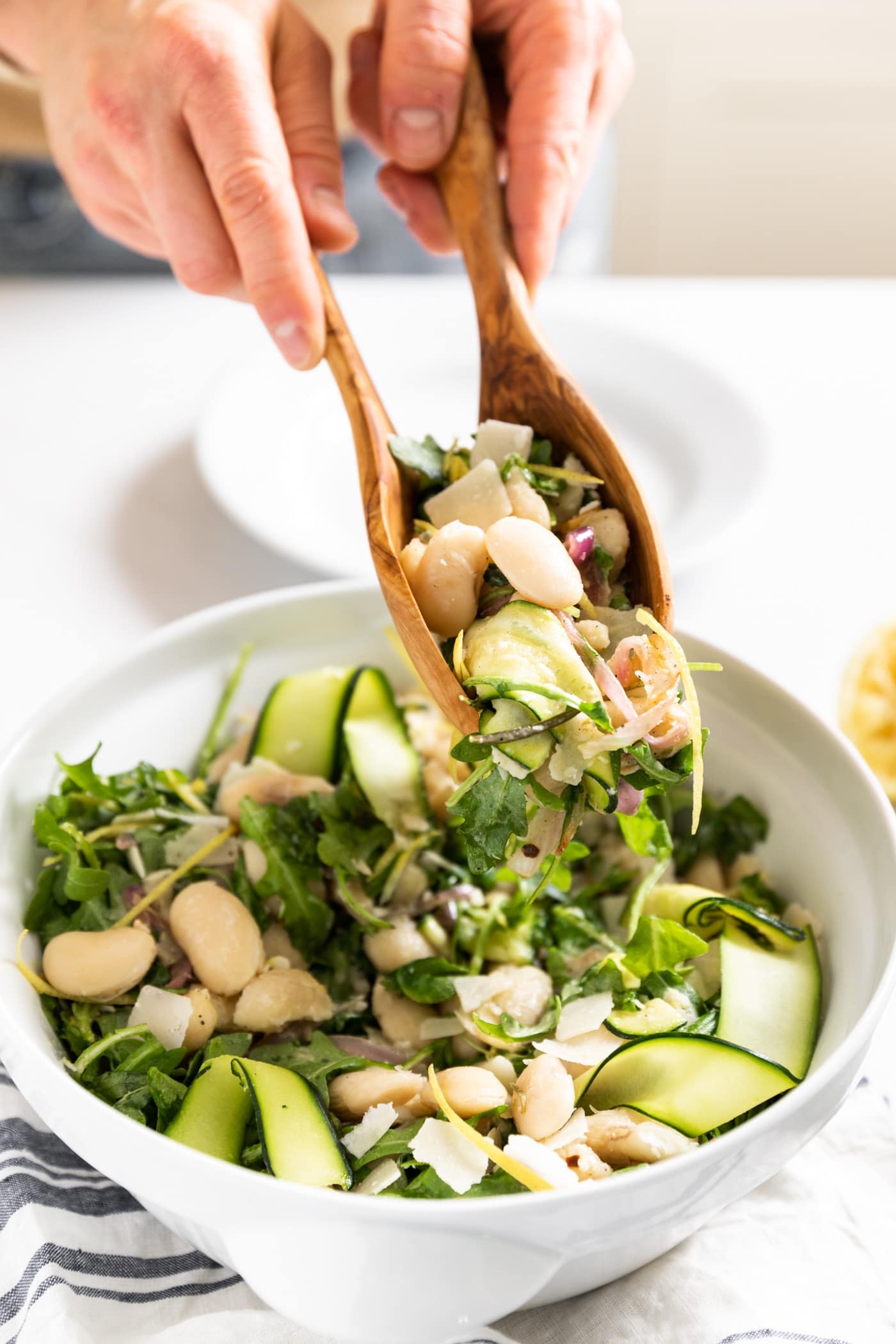Close up view of large white bowl with two wood tongs holding a combination of white beans and greens