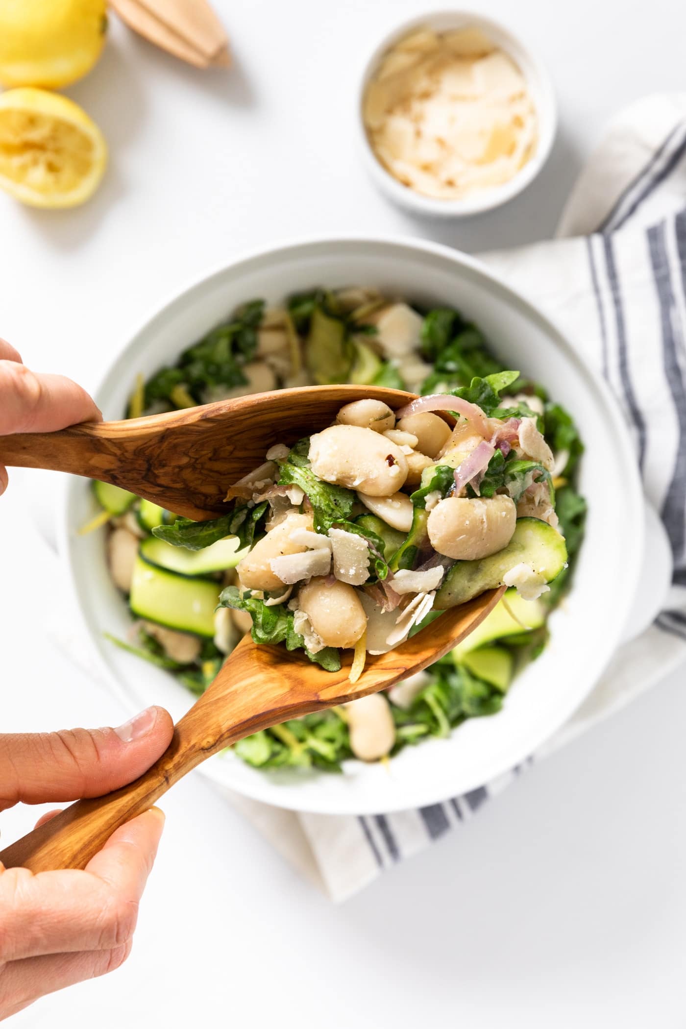 Top down view of wooden utensils holding a serving of white beans mixed with greens with rest of salad below