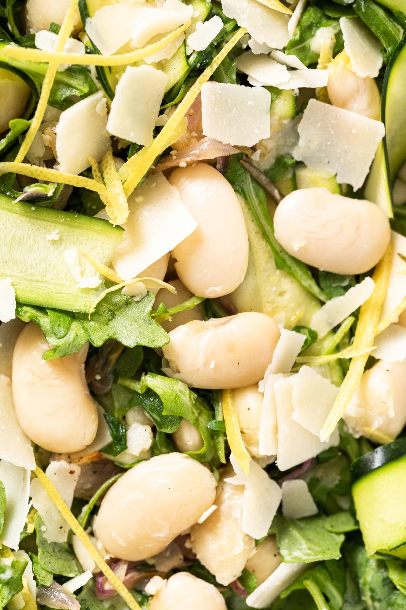 Close up view of large white beans nestled among greens and Parmesan and lemon zest