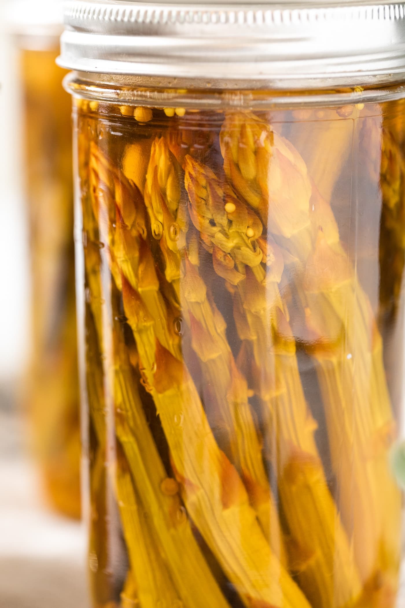 Close up view of pickled asparagus spears in glass jar with ring on top