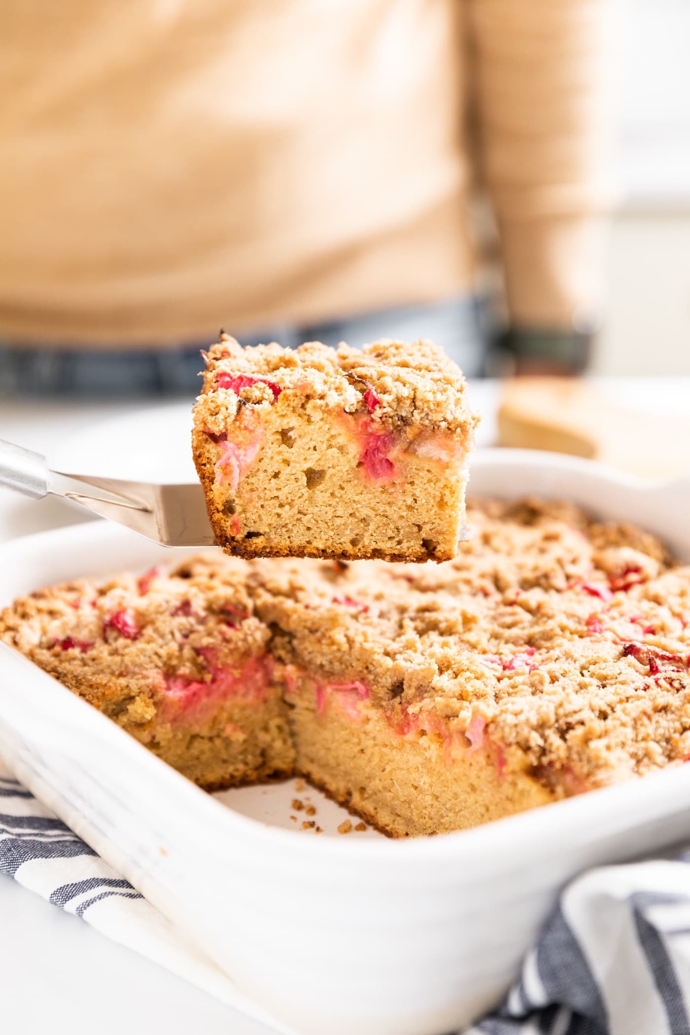 Side view of piece of rhubarb coffee cake after being pulled from white baking dish being held by hand