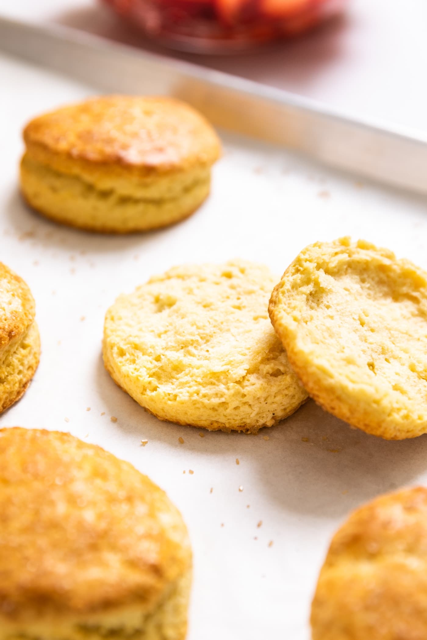 Sliced biscuit with both halves sitting close to each on baking dish with other unsliced biscuits around