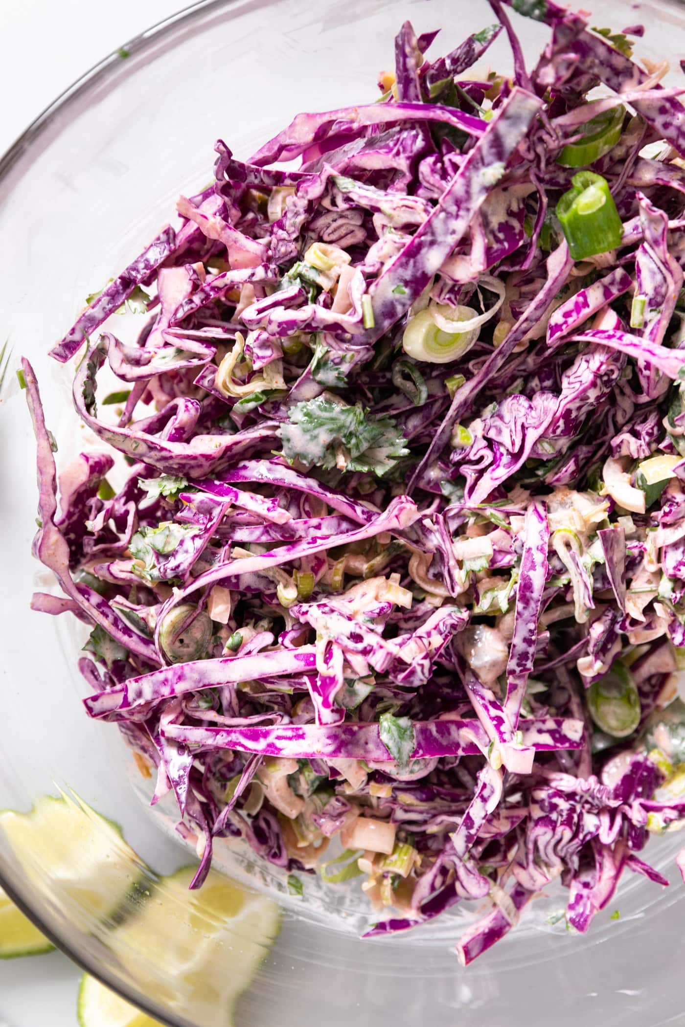 Top down view of purple cabbage made into coleslaw with white colored dressing poured over top all in glass bowl