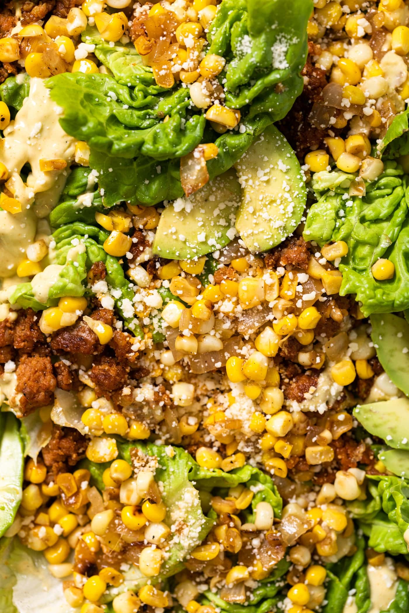Top down close up view of big pieces of green lettuce topped with sweet corn and chorizo pieces after being cooked and topped with creamy taupe colored dressing