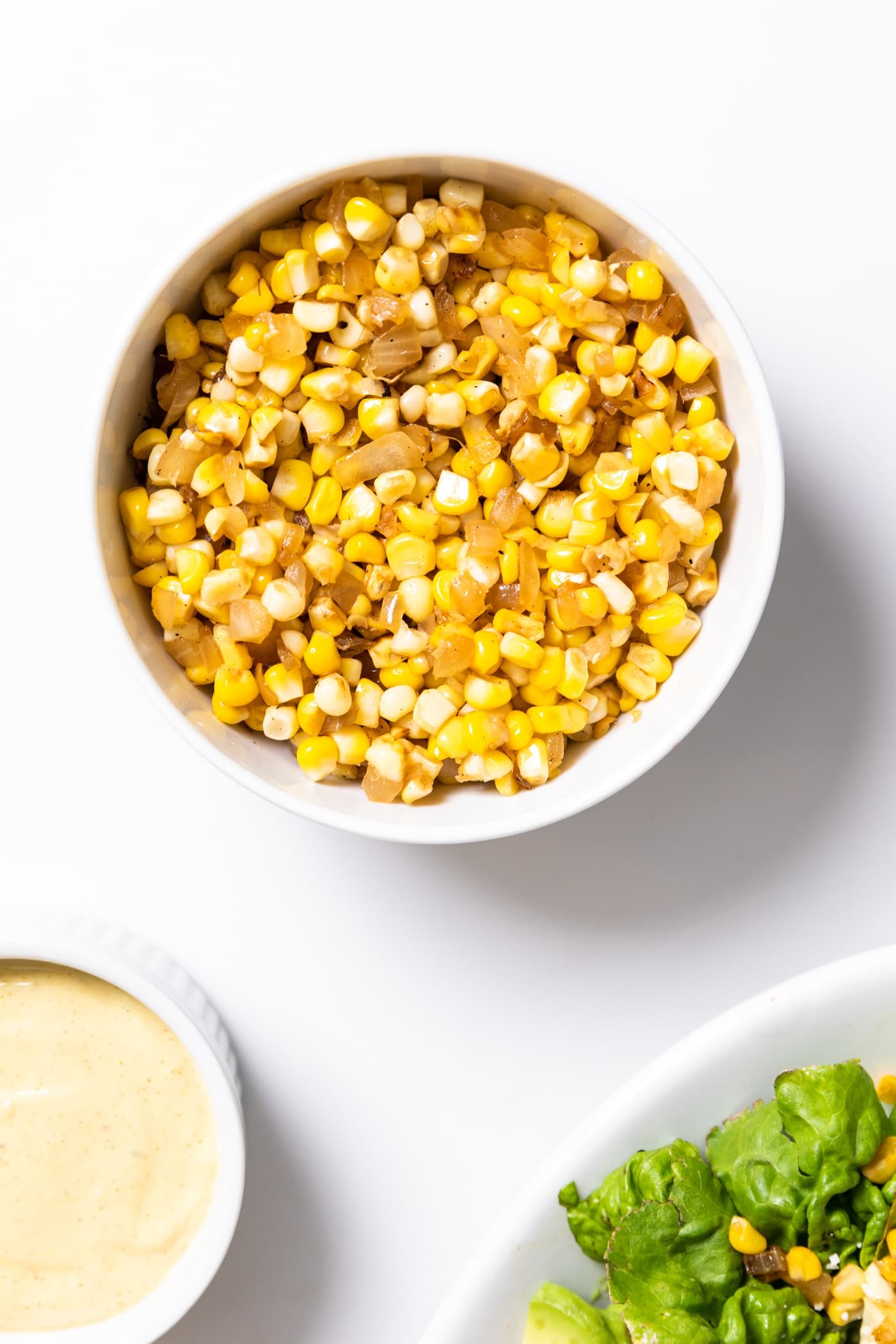 Top down view of cooked combination of sweet corn and onion sitting in white bowl after being on the stove