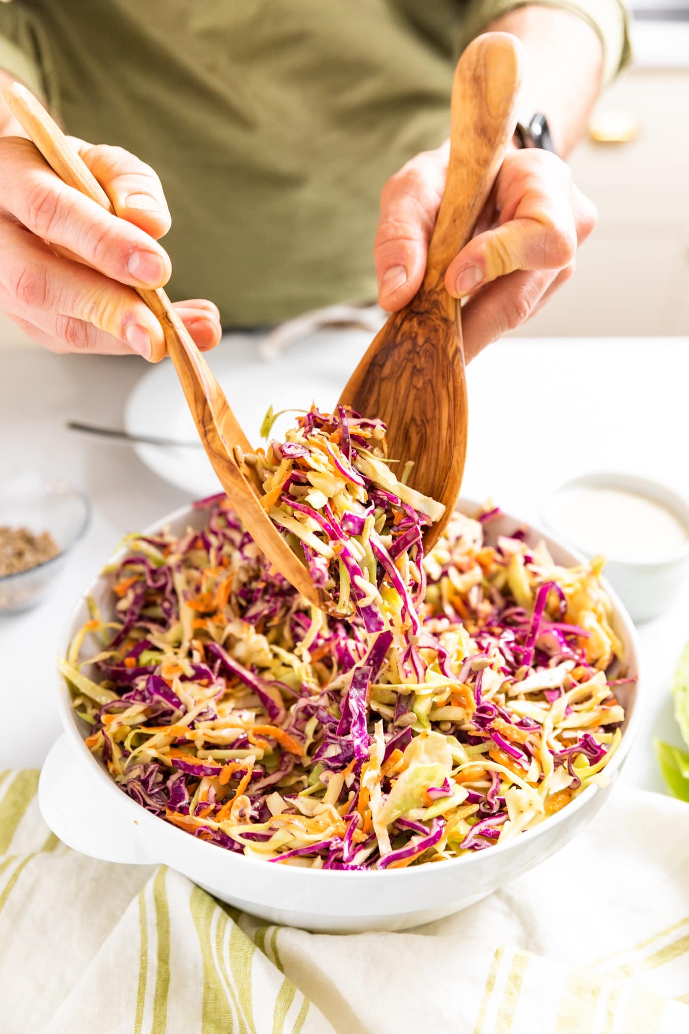 Two hands holding wooden tongs picking up red and green colored coleslaw