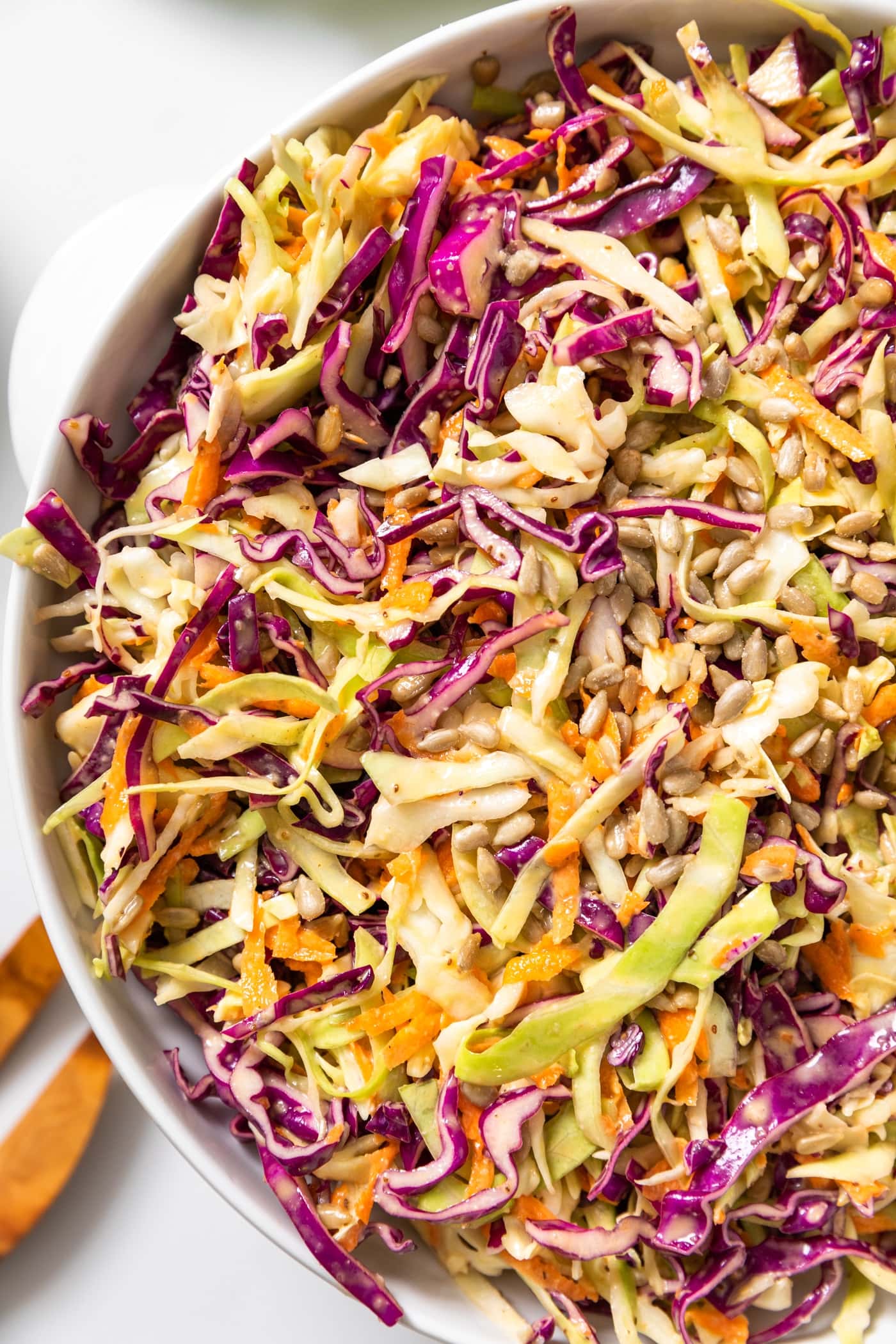 Top down view of white bowl with green and purple cabbage mixed with carrots sitting on white countertop
