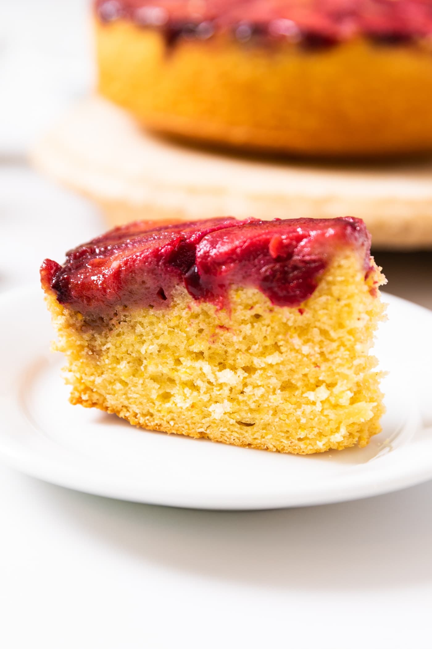 Side view of yellow colored cornmeal cake with a plum layer topping sitting on white plate with rest of cake in background