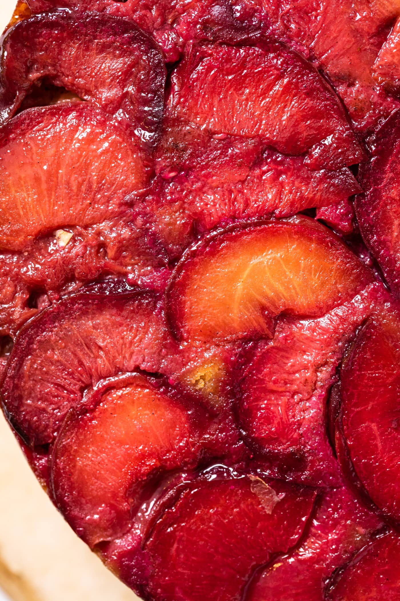 Top down close up view of slices of baking plum sitting on top of cornmeal cake with bright reds and light yellows
