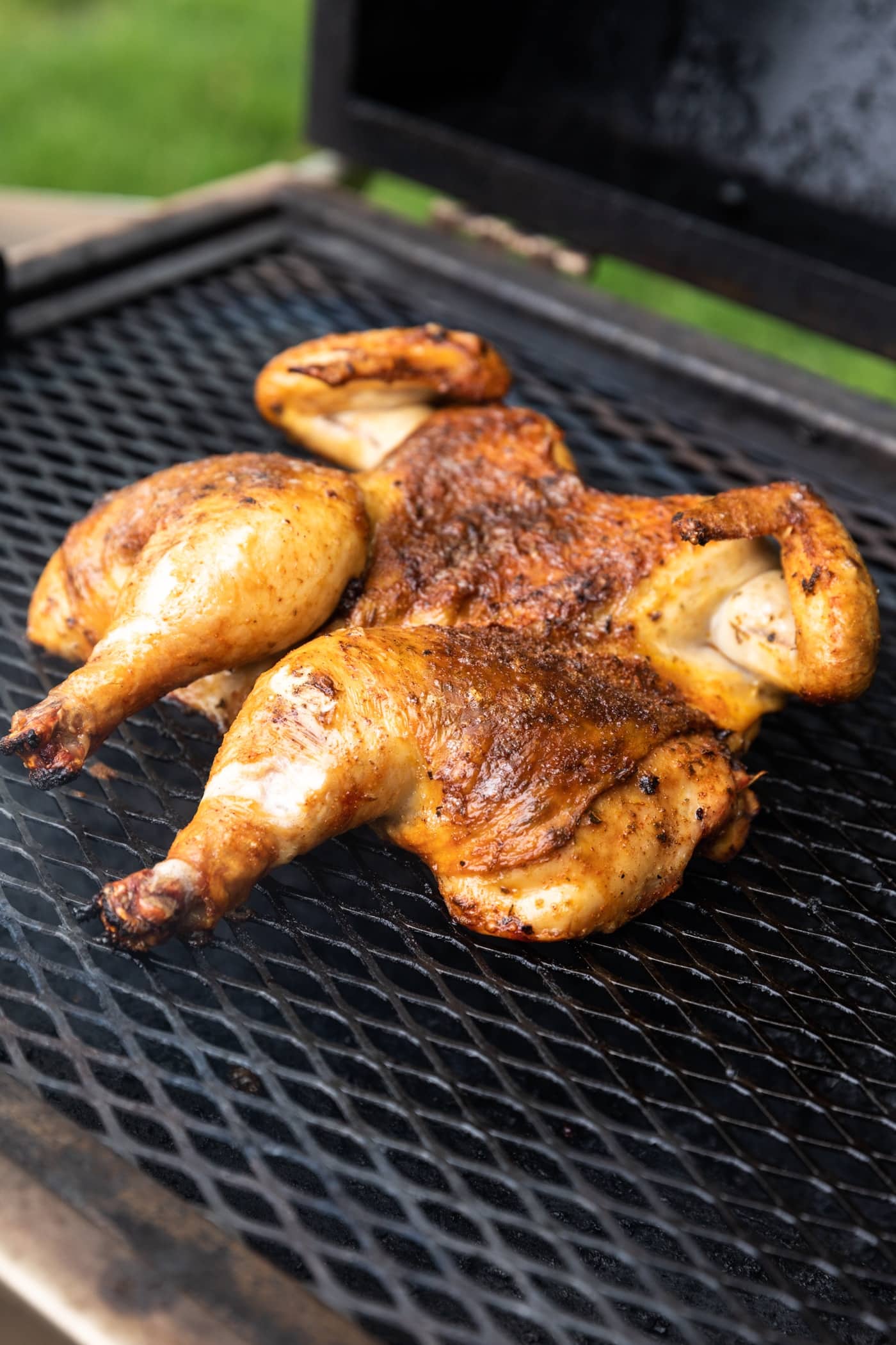 Orange colored chicken sitting on grill with lid open with green grass in background