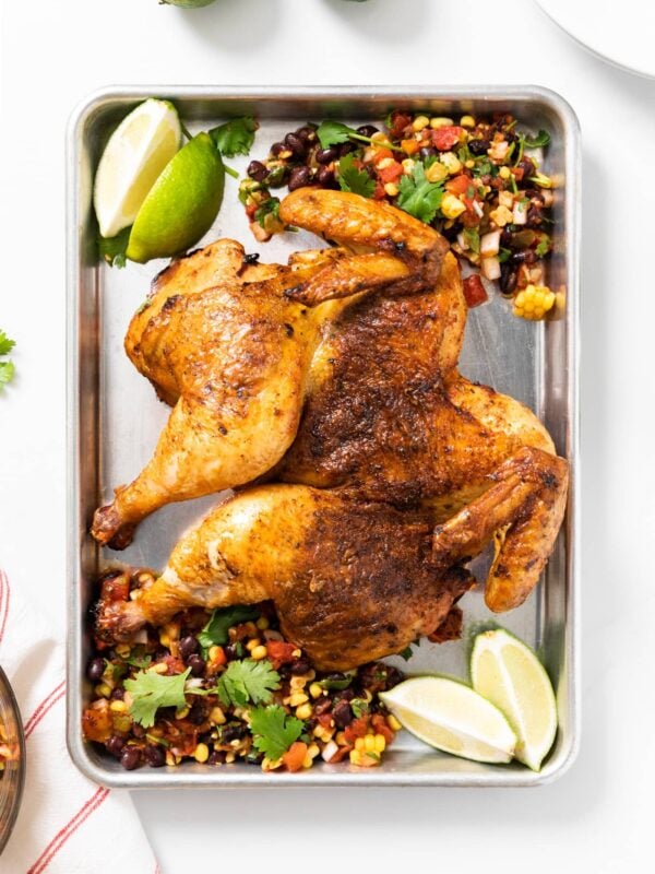 Top down view of steel pan sitting on white countertop with grilled orange colored chicken with slices of lime and chunky salsa
