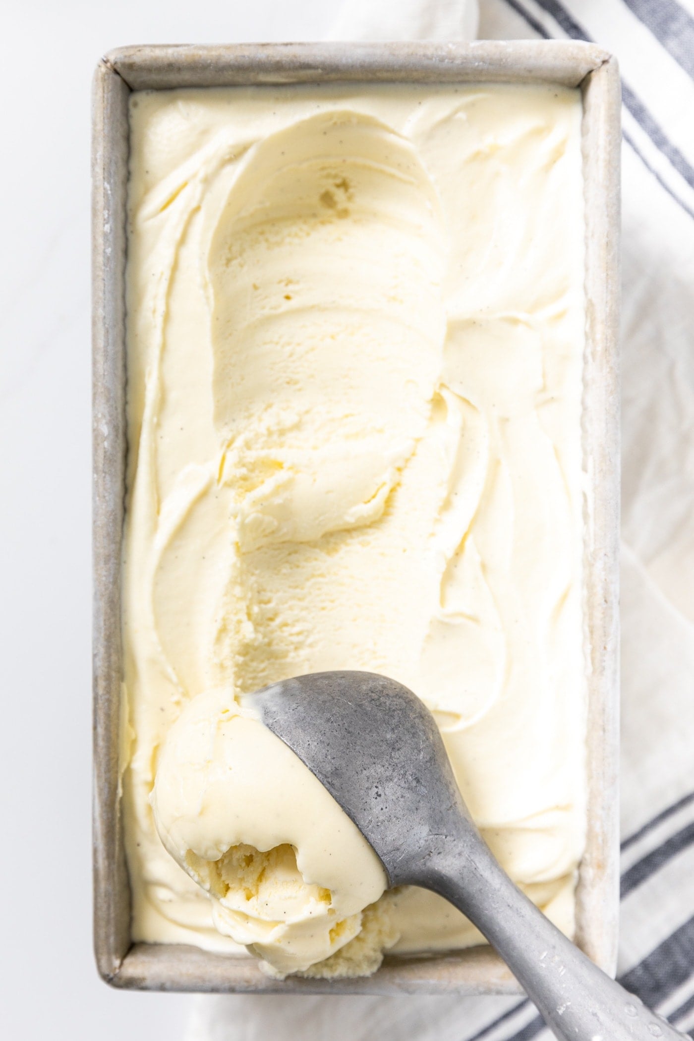 Close up view of ice cream scoop scooping vanilla ice cream from silver container in which it was frozen