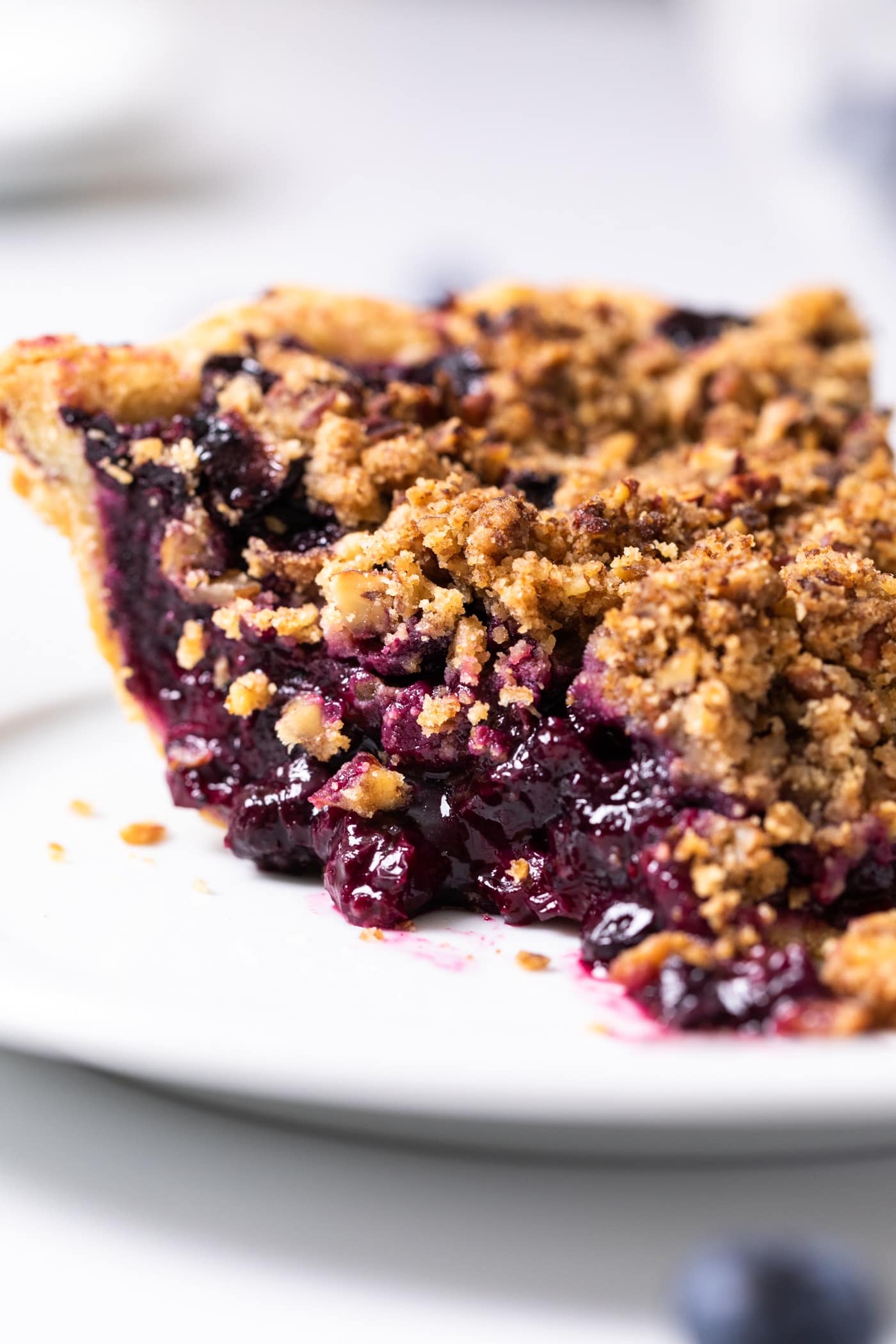 Side angle view of slice of blueberry pie with streusel topping all on white plate on white countertop