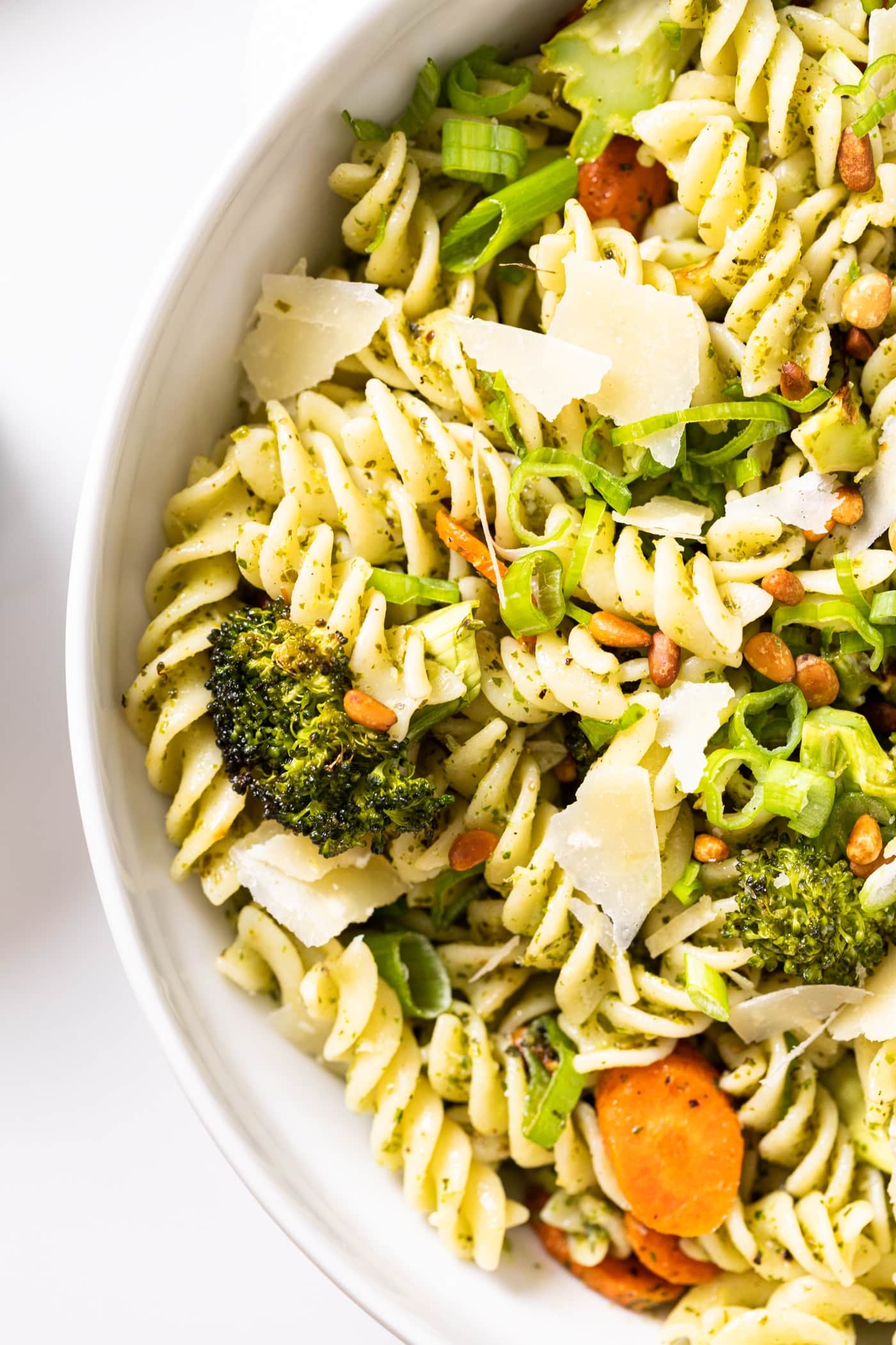 White bowl filled with pasta and carrots and broccoli and topped with Parmesan cheese and pine nuts