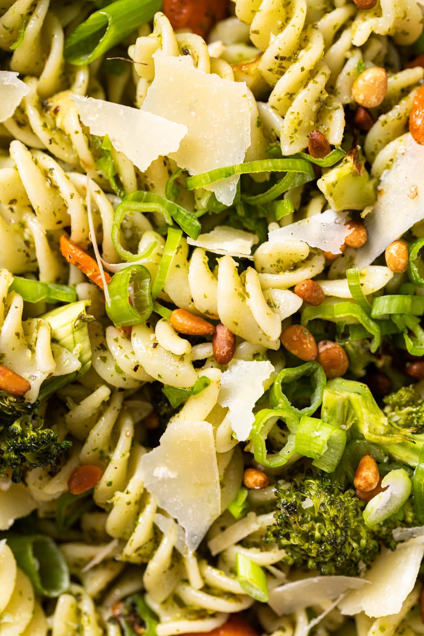 Close up view of cooked yellow pasta nestled with pieces of Parmesan cheese and broccoli and pine nuts