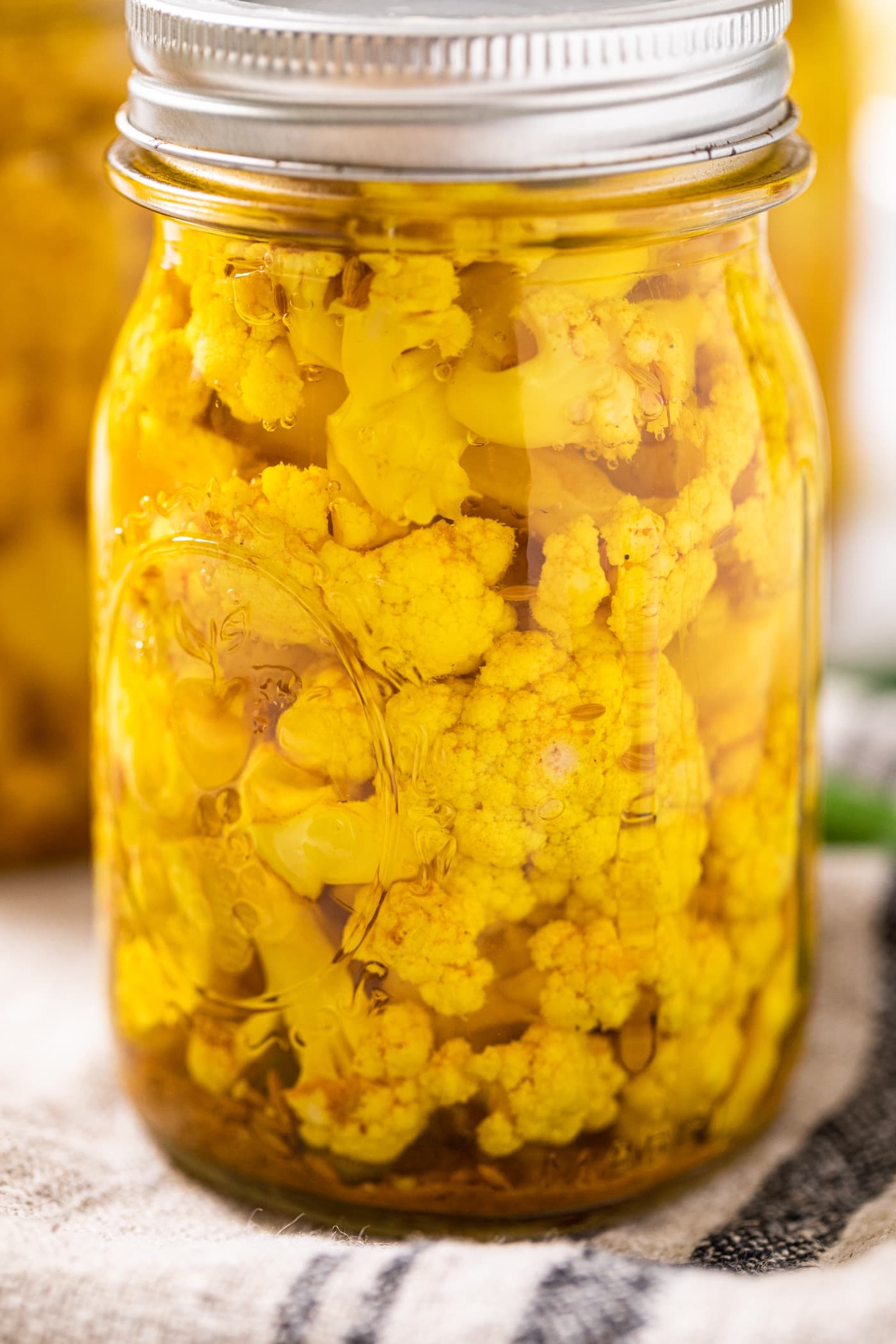 Close up view of side of curry cauliflower sitting in glass jar with lid and ring on top with towel underneath