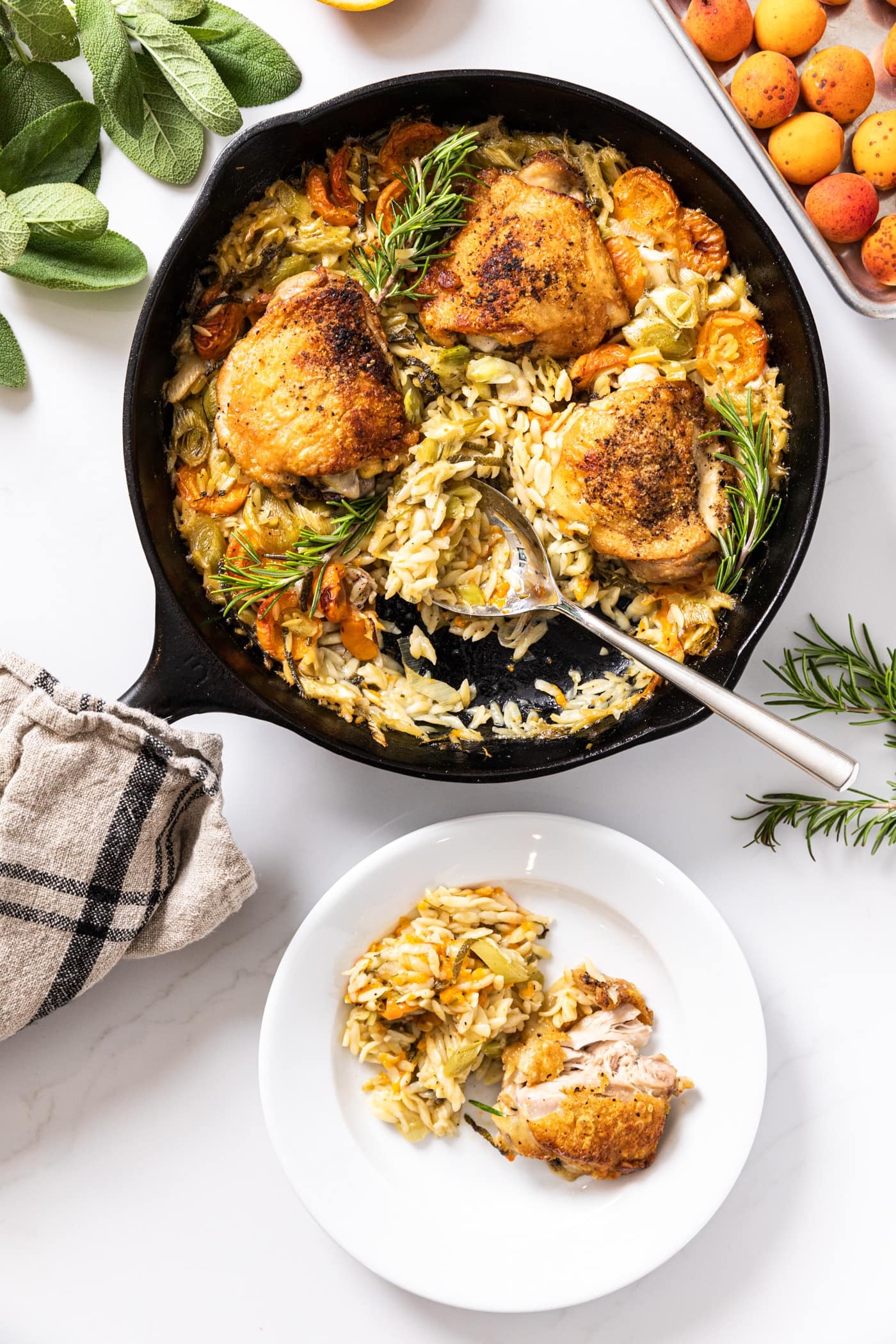 Top down view of black skillet with spoon sitting after taking scoop out and putting on white plate filled with orzo and chicken all on white countertop