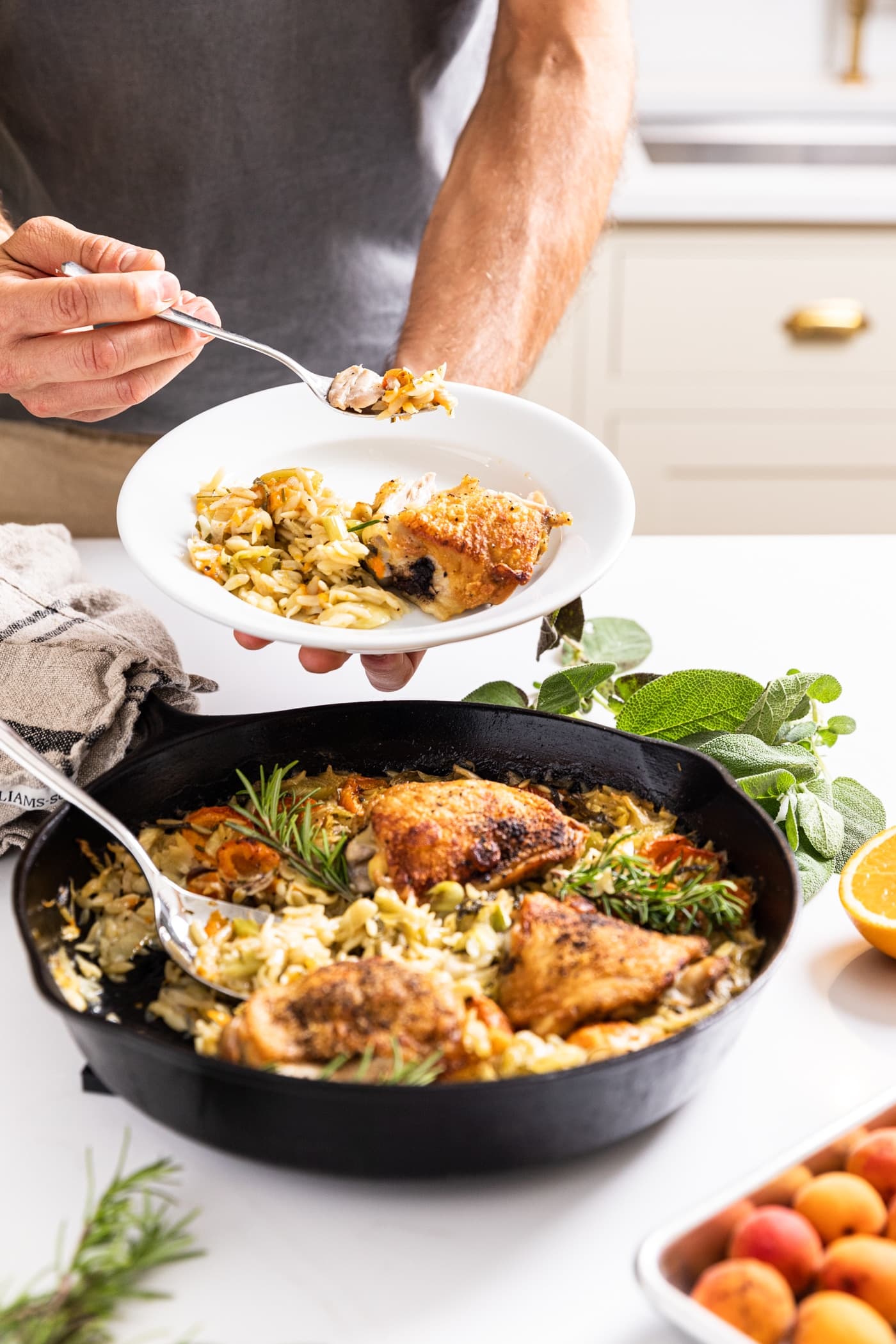 Two hands holding white plate with fork holding piece of chicken after being scooped out of skillet underneath