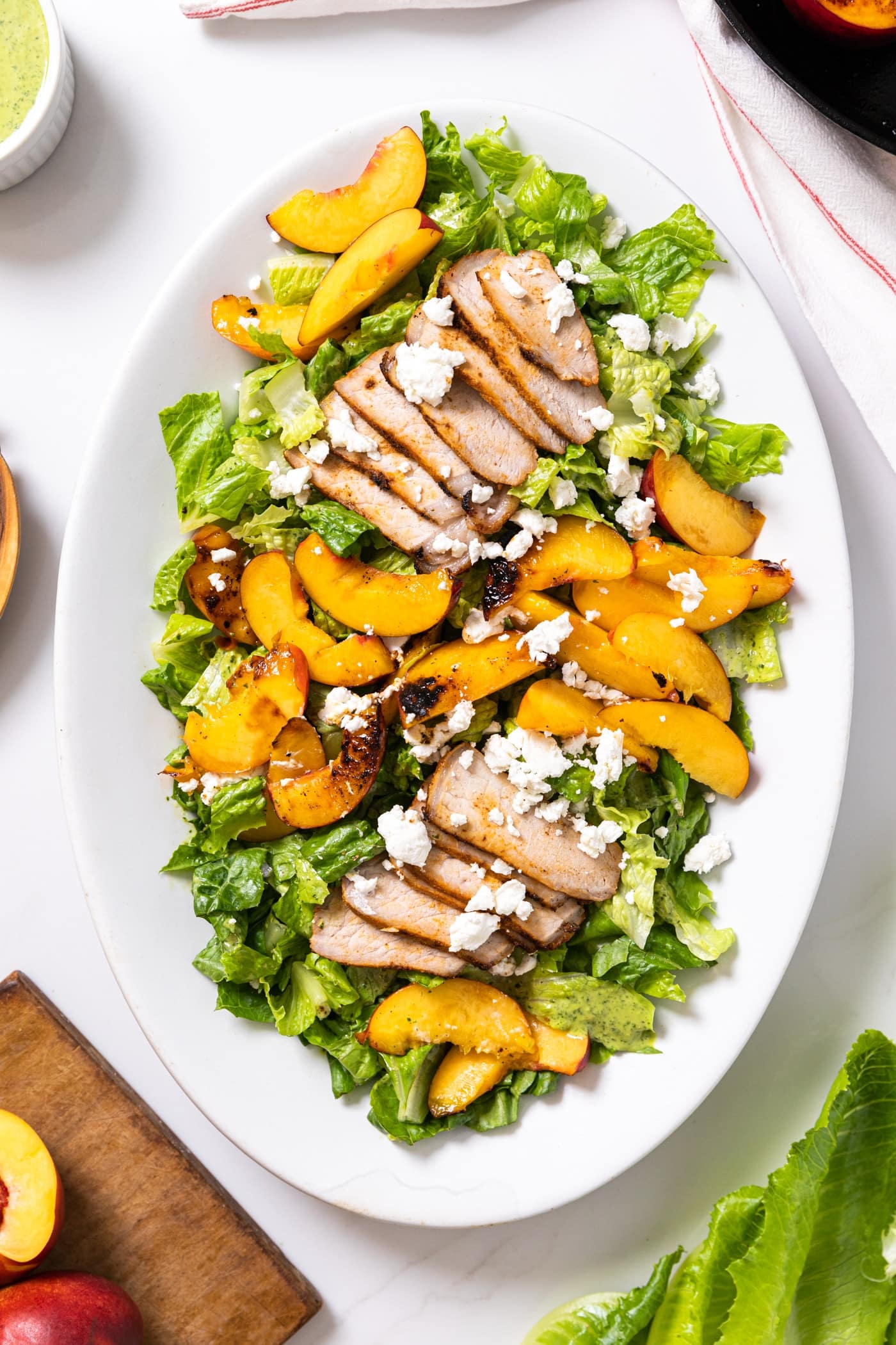 Top down view of white platter sitting on white countertop with lettuce and sliced pork and slices of nectarine