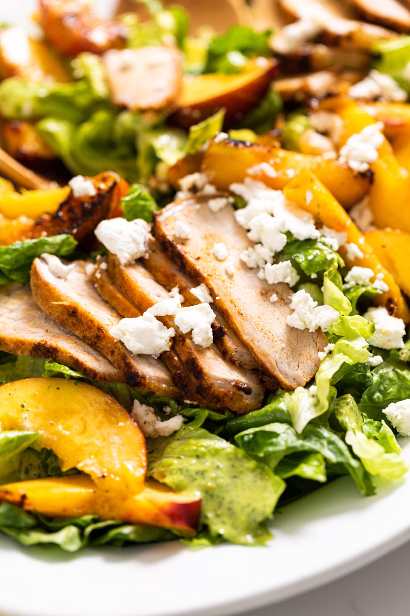 Close up view of white plate filled with lettuce topped with slices of pork and nectarines with goat cheese on top