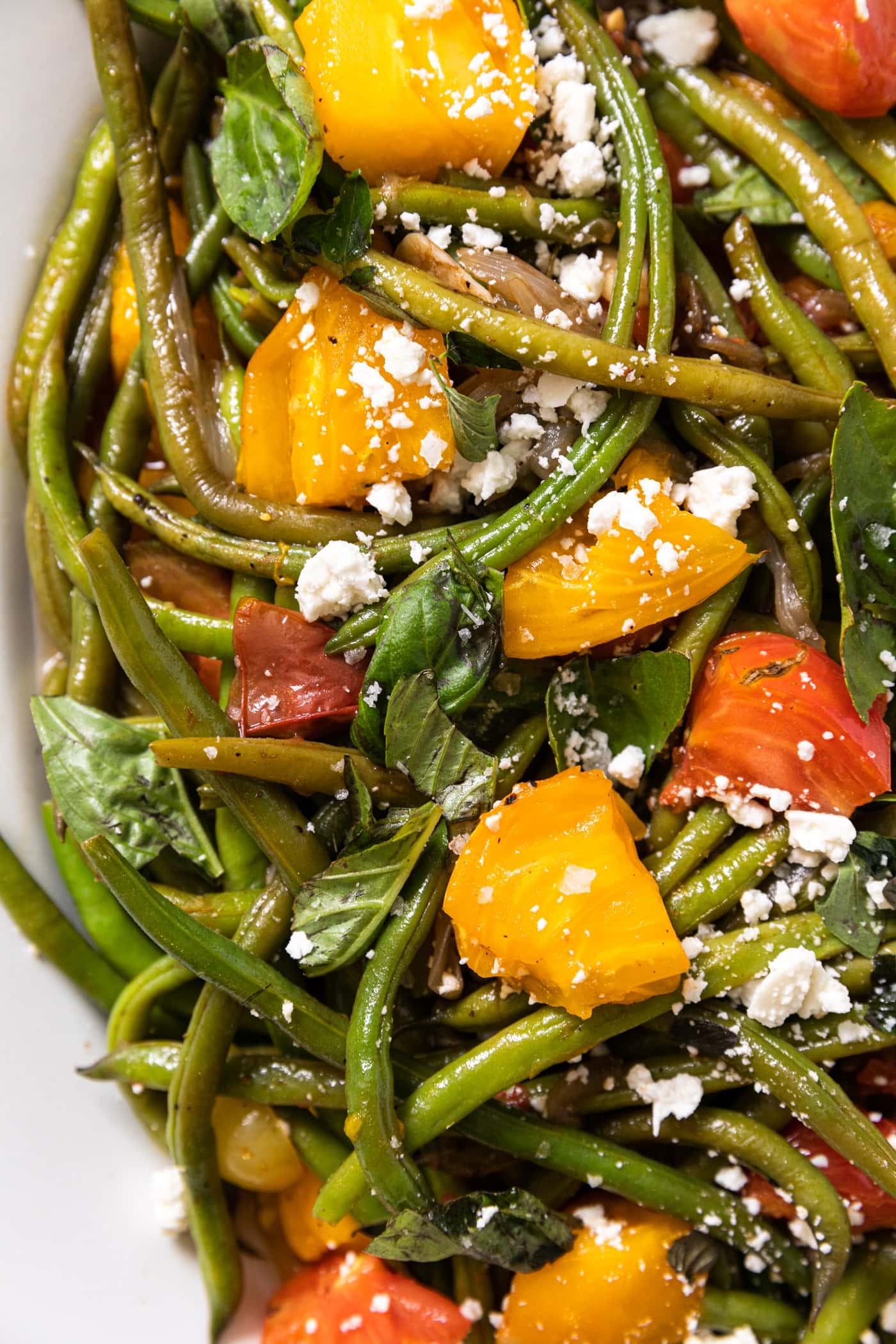 Top down view of white platter filled with green beans and topped with yellow and red tomatoes and topped with a sprinkling of feta cheese