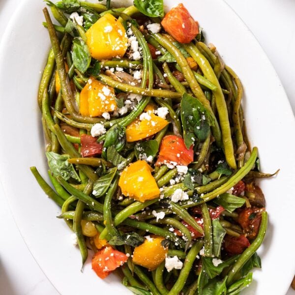 Top down view of white platter packed full of green beans topped with roasted red and yellow tomatoes with sprinkling of feta cheese across the top